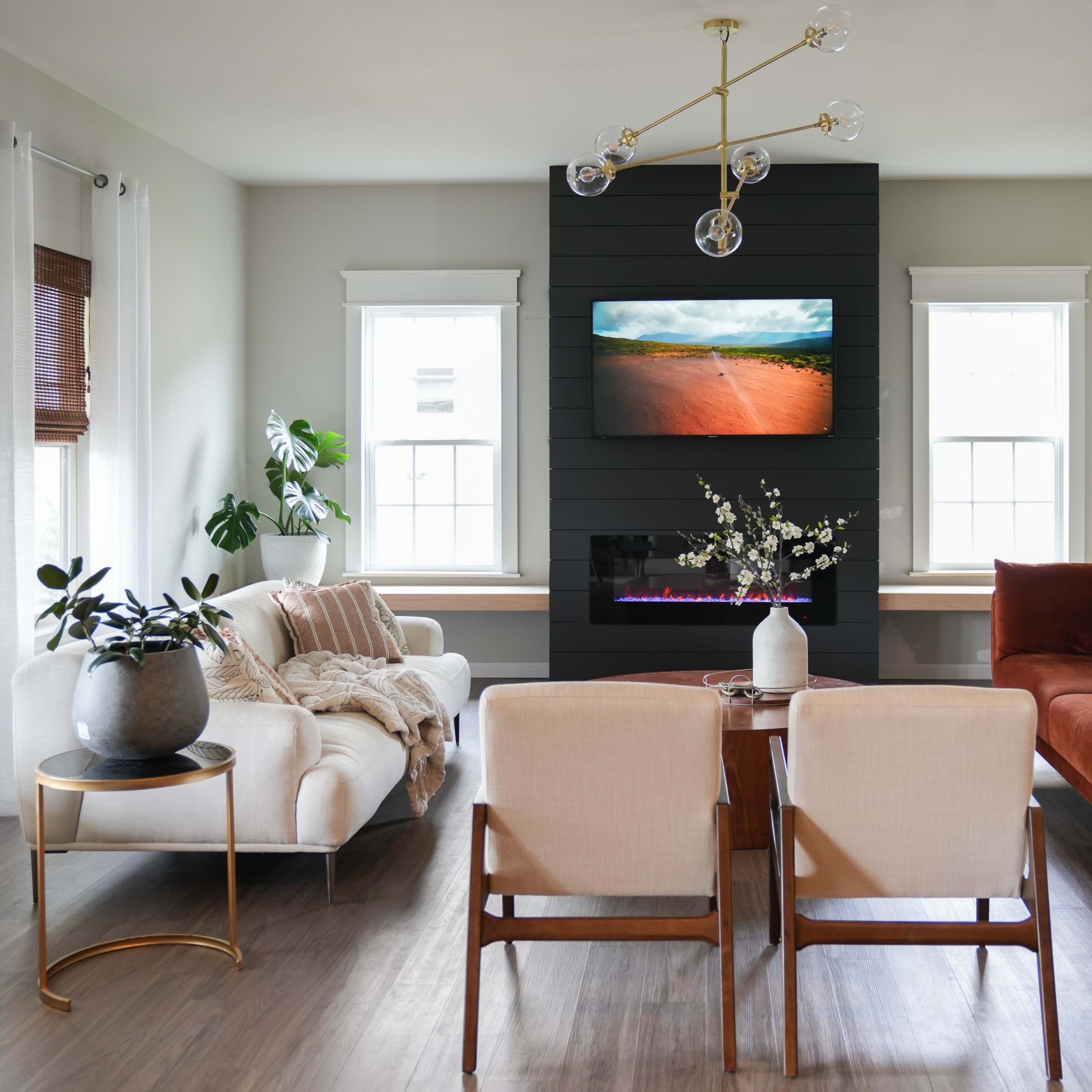 A modern living room features a dark accent wall with a mounted TV, two sofas, a coffee table, and large windows letting in natural light.