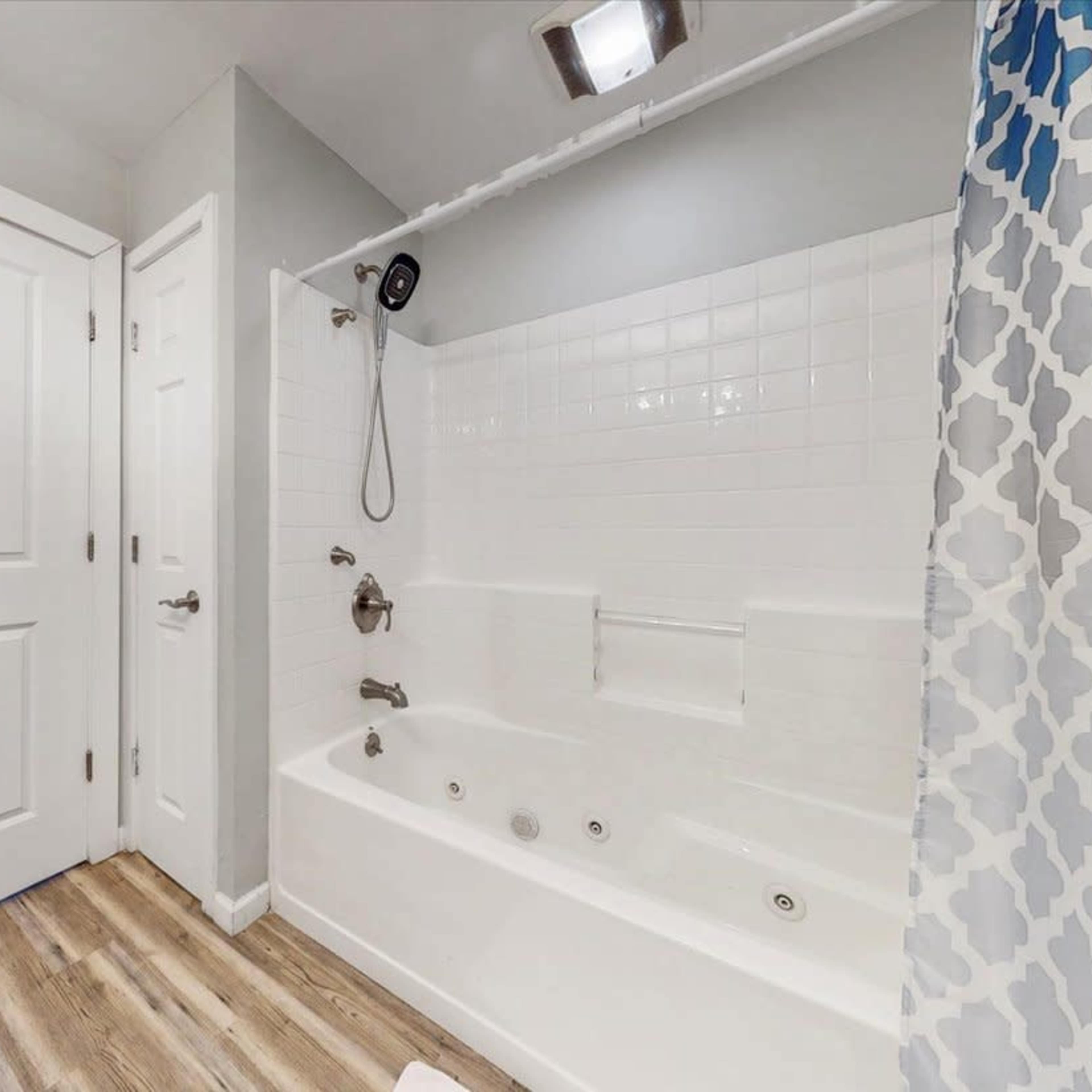 A bathroom with a shower and bathtub combination, white tile walls, and a gray patterned shower curtain.