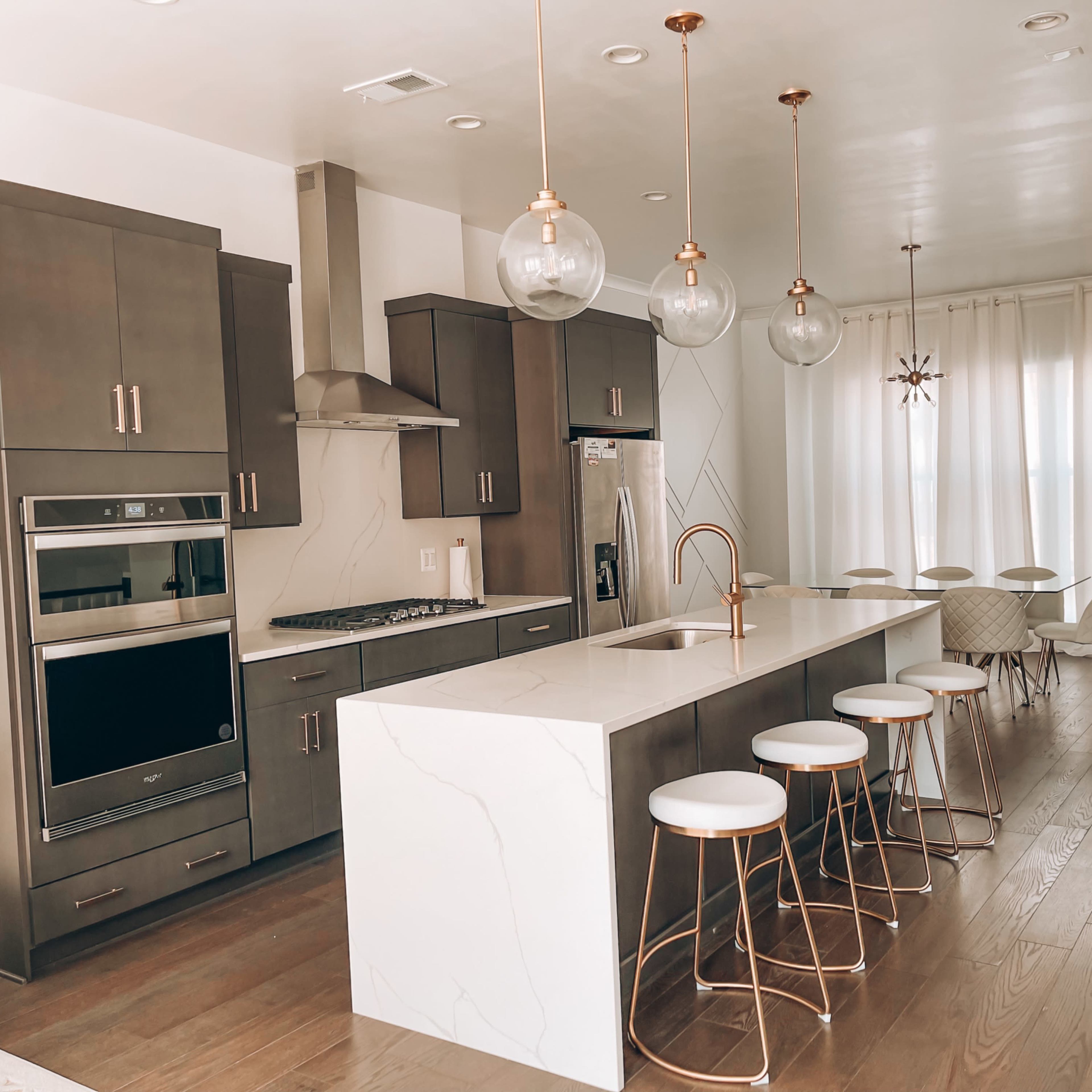 A modern kitchen with dark cabinets, a large marble island with seating, and pendant lights above.