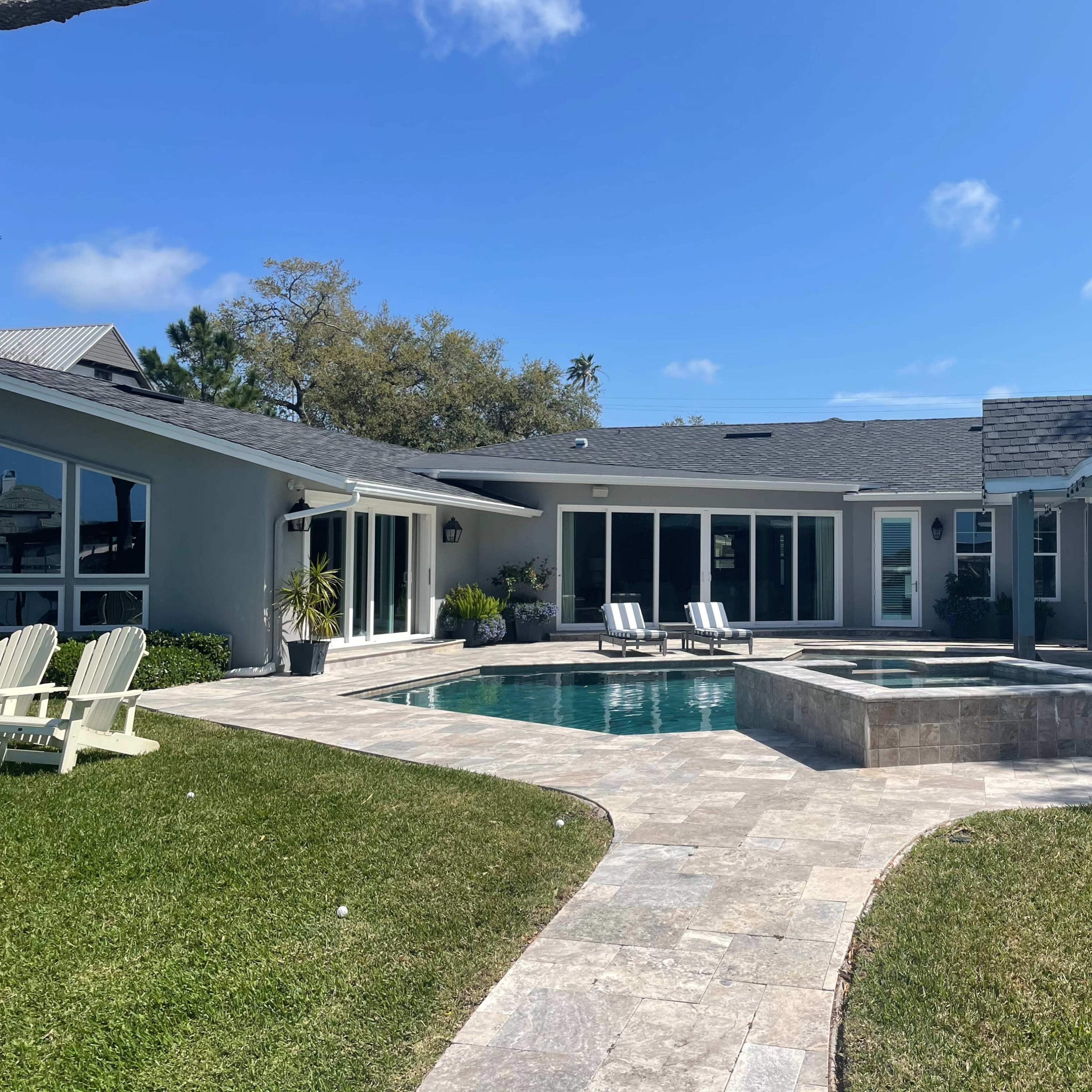 A modern house with a swimming pool and a stone patio surrounded by green grass and trees.
