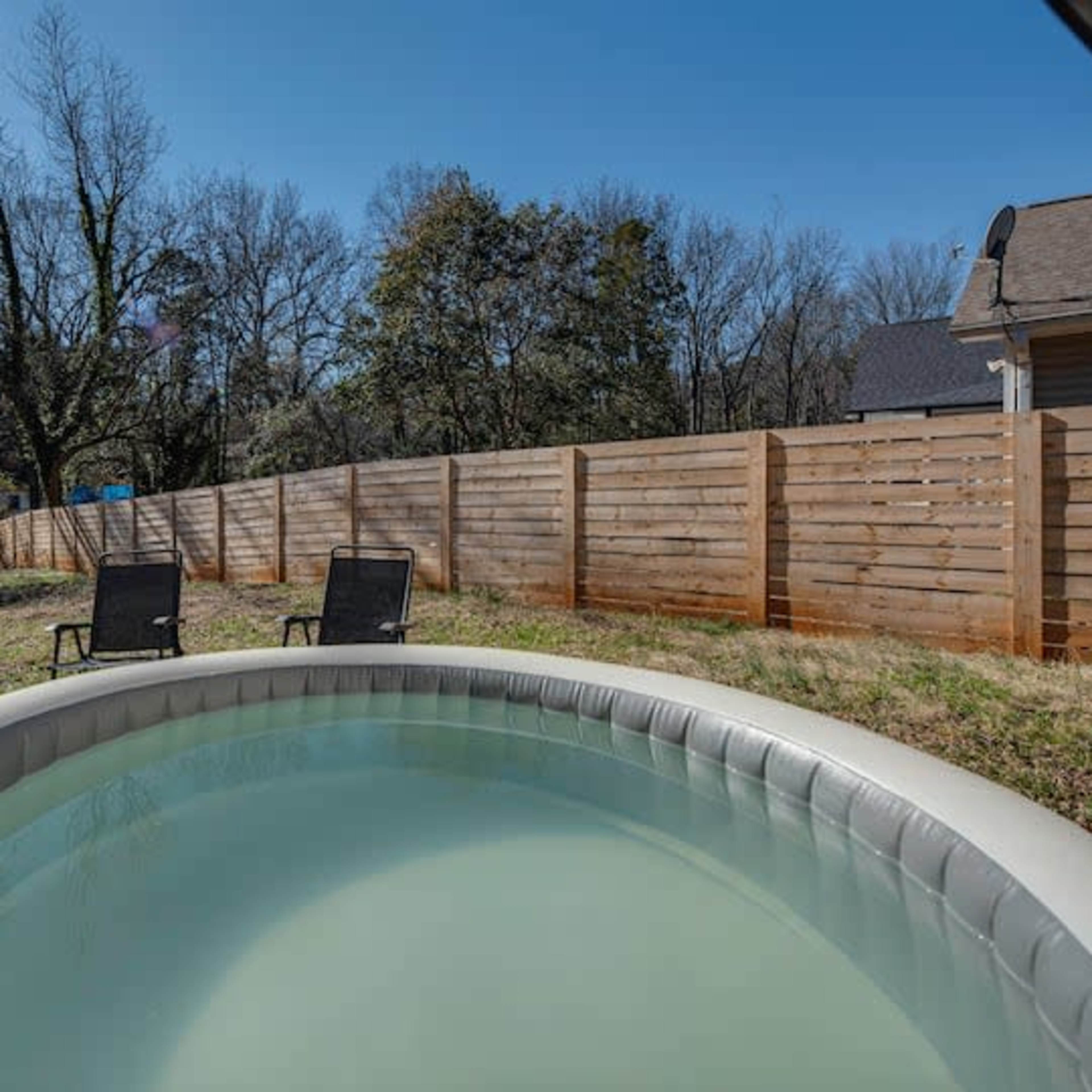 A small inflatable pool is set up in a backyard with two chairs and a wooden fence in the background.