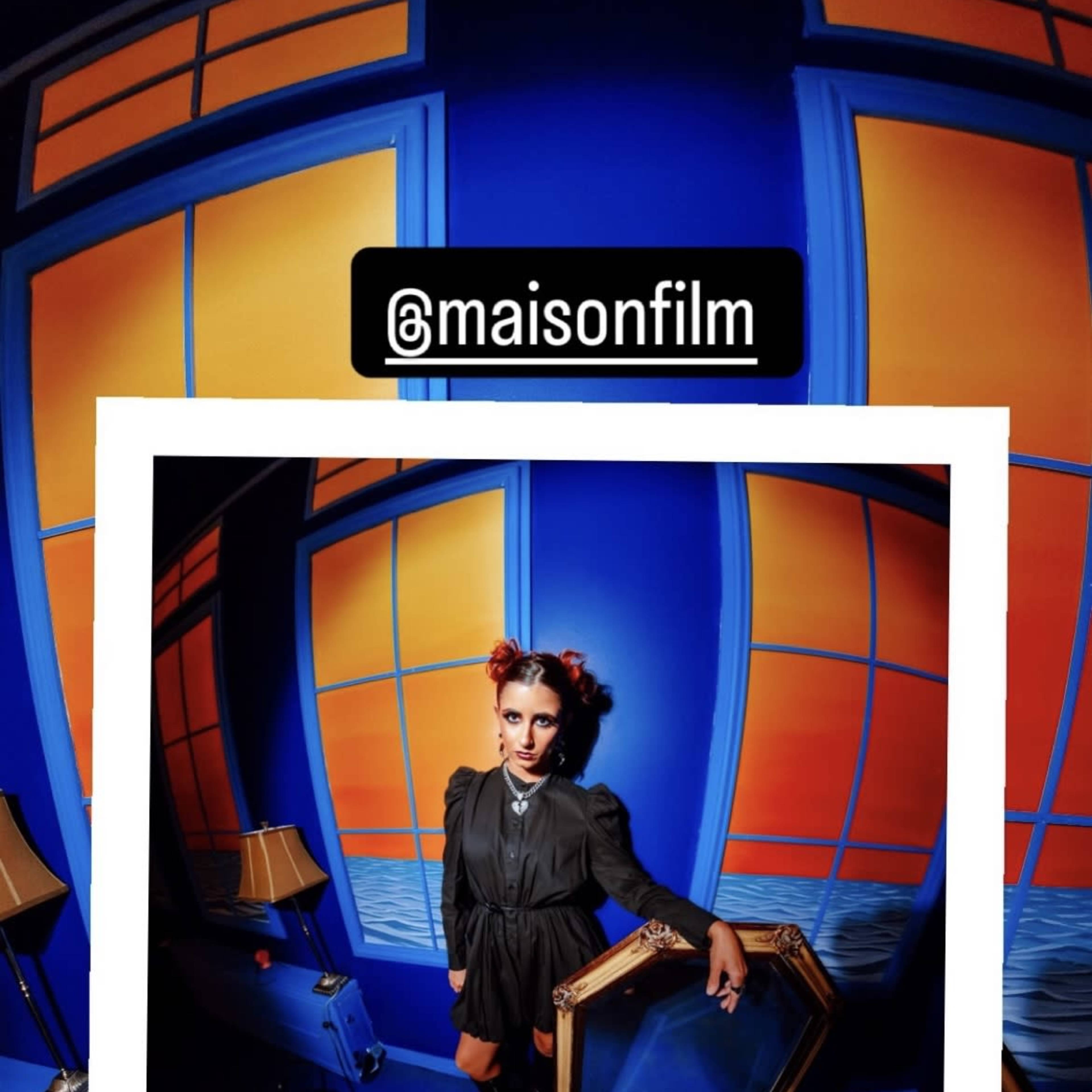 A person in a dark outfit poses in front of a brightly colored blue and orange background at Maison Film Studios.
