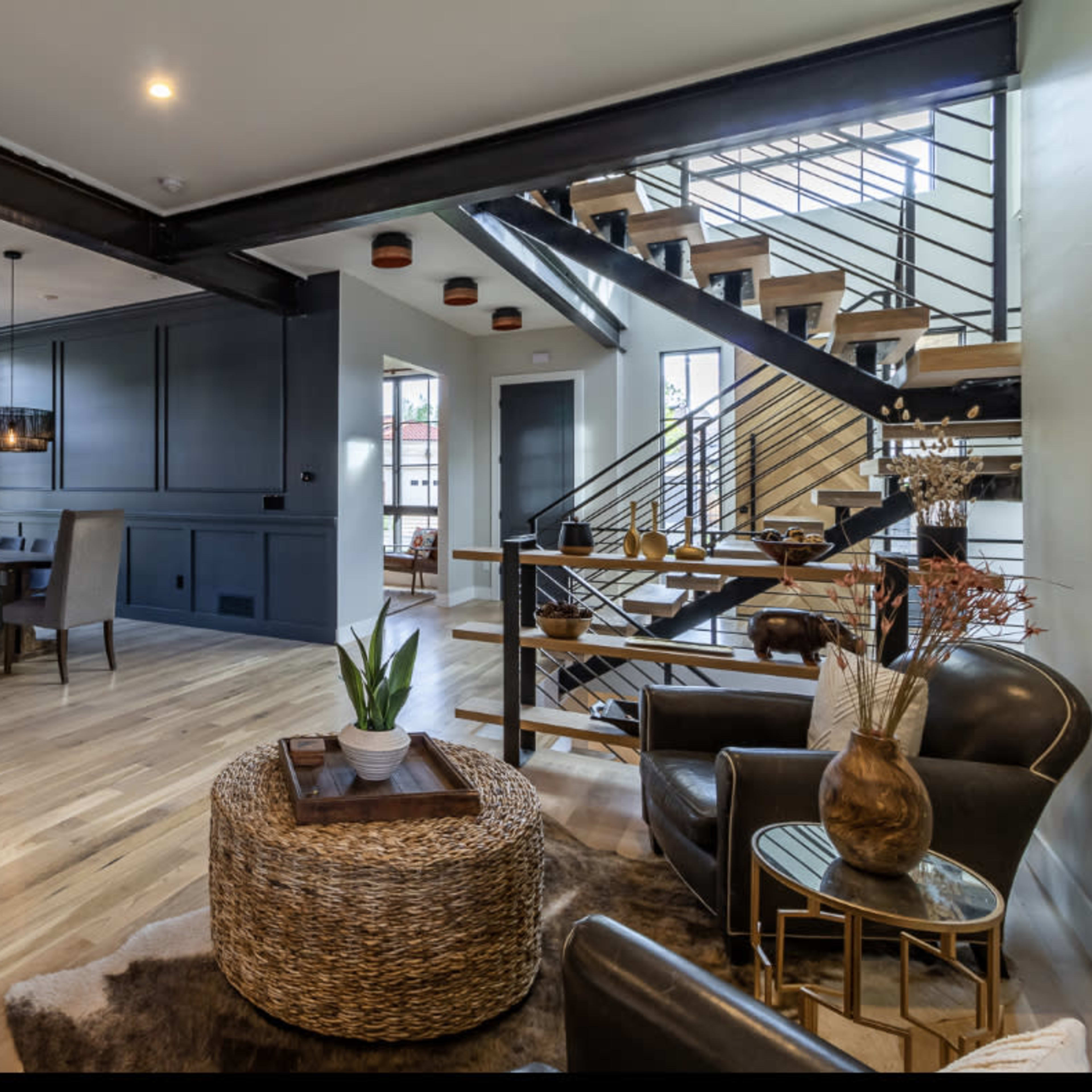 A modern interior featuring a wooden staircase, a seating area with leather chairs, and a dining space with a dark wall and decorative accents.