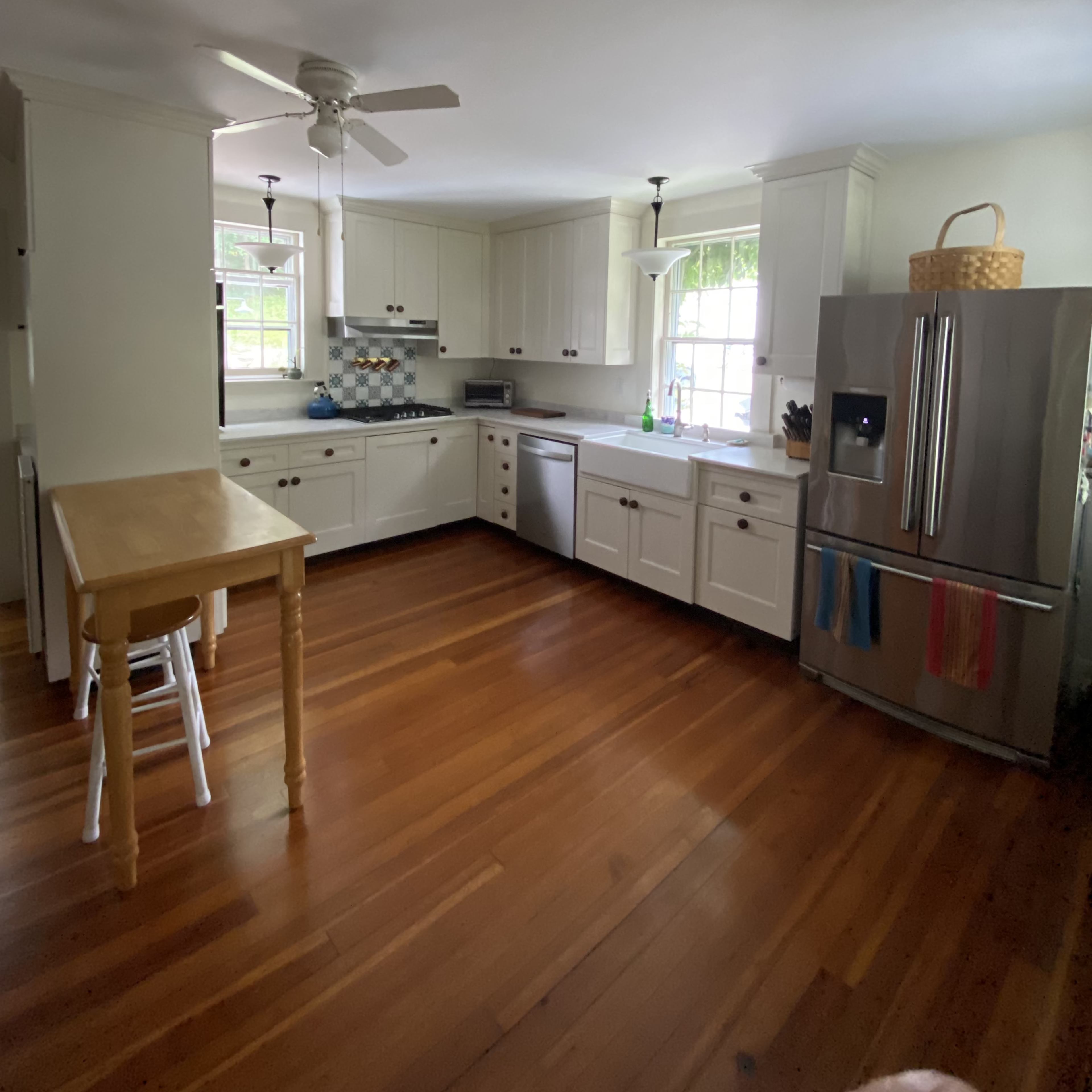 A spacious kitchen features white cabinetry, a stainless steel refrigerator, a wooden table, and hardwood flooring.