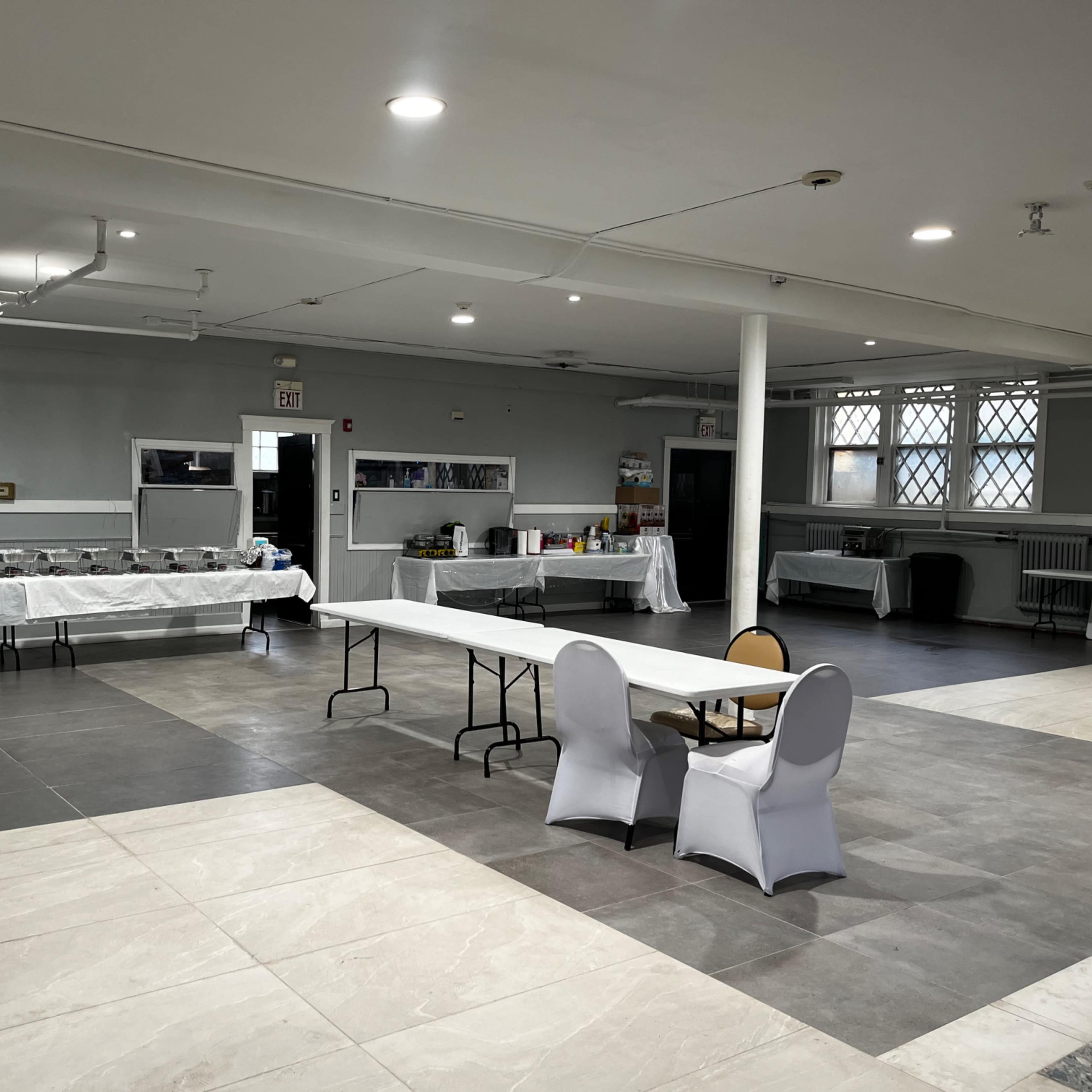 A spacious indoor venue with a long table set for a buffet and a small seating area featuring a table and two chairs.