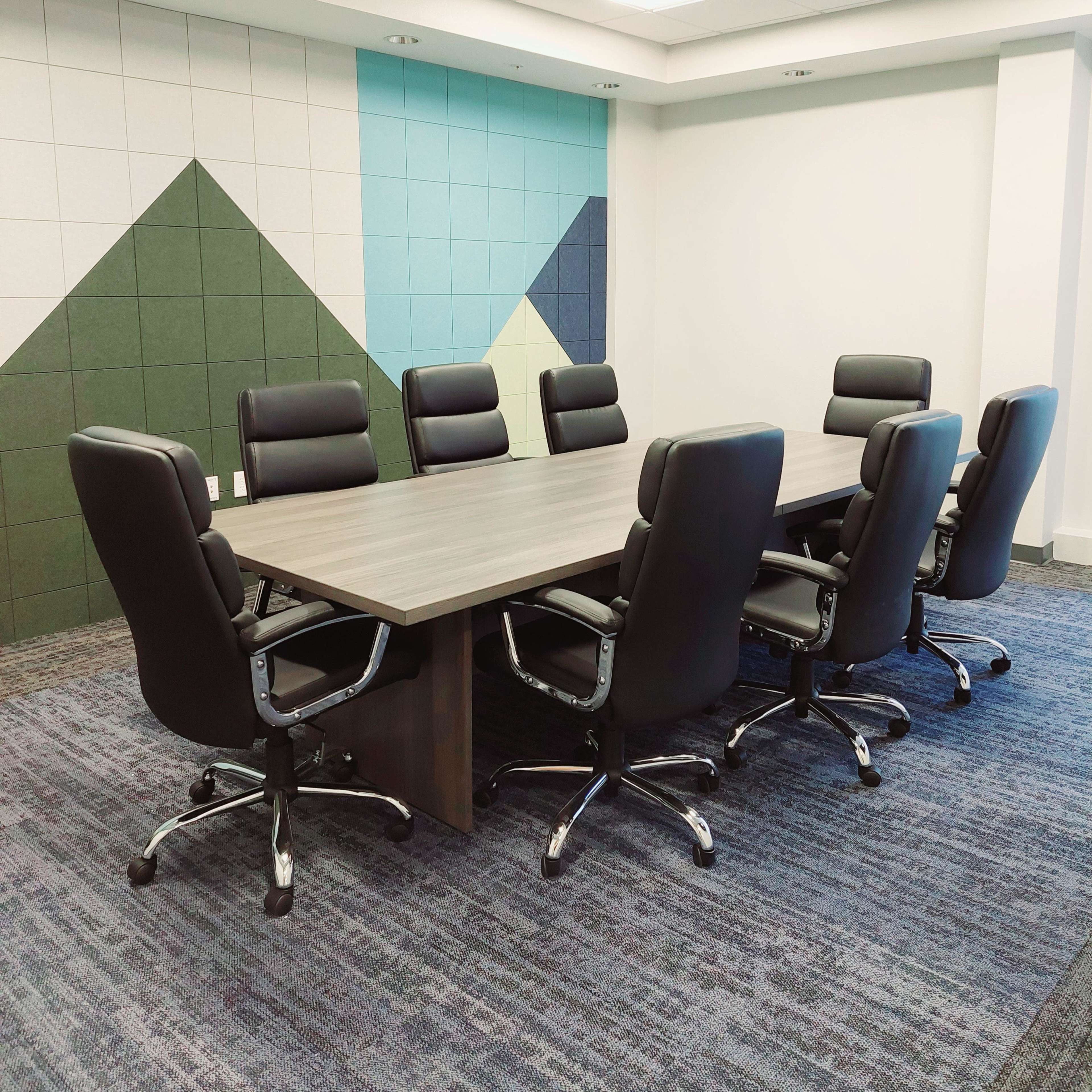 A modern conference room features a large table surrounded by eight black ergonomic chairs, set against a backdrop of colorful geometric wall designs.