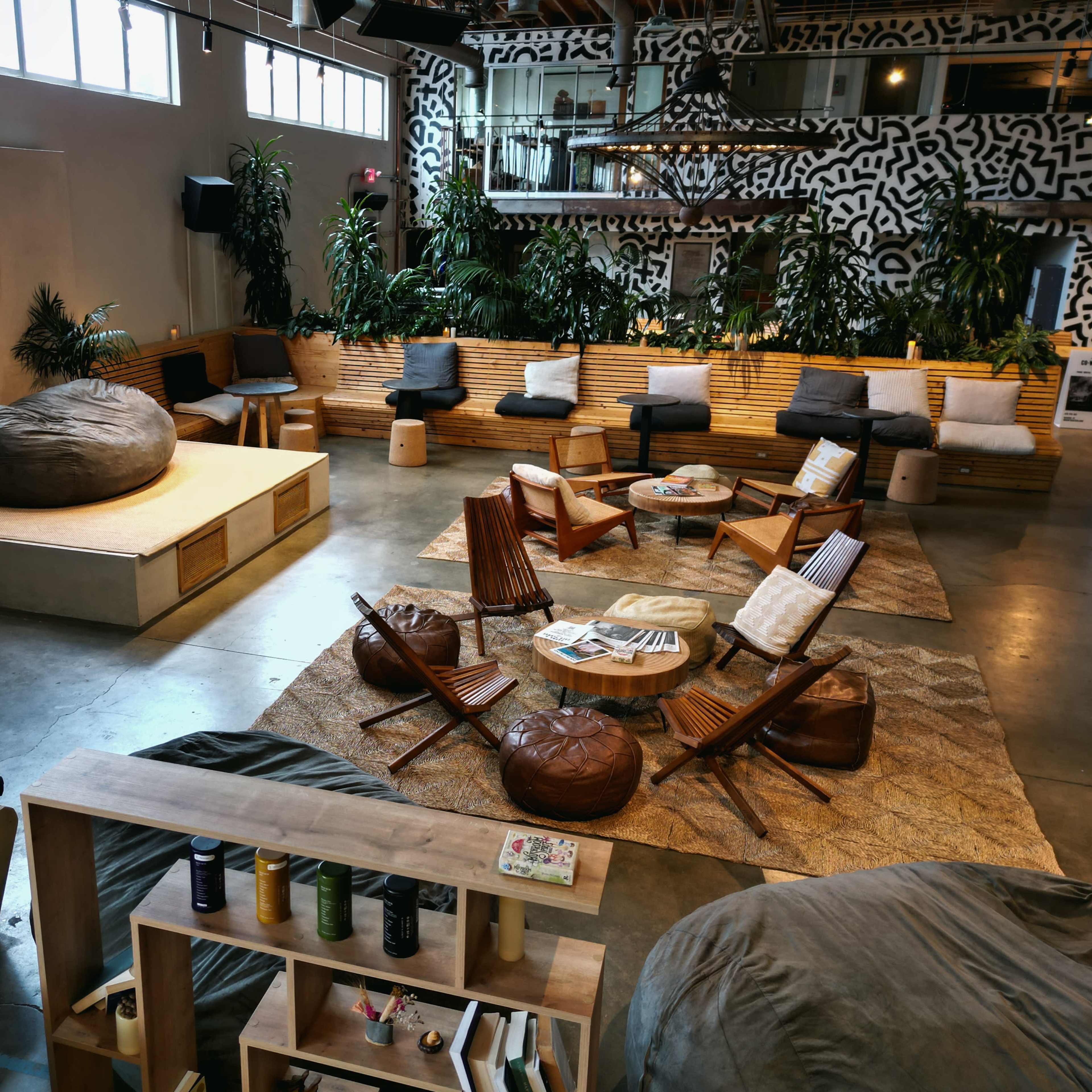 A spacious lounge area with wooden seating, large bean bags, circular tables, and plants, creating a relaxed atmosphere.