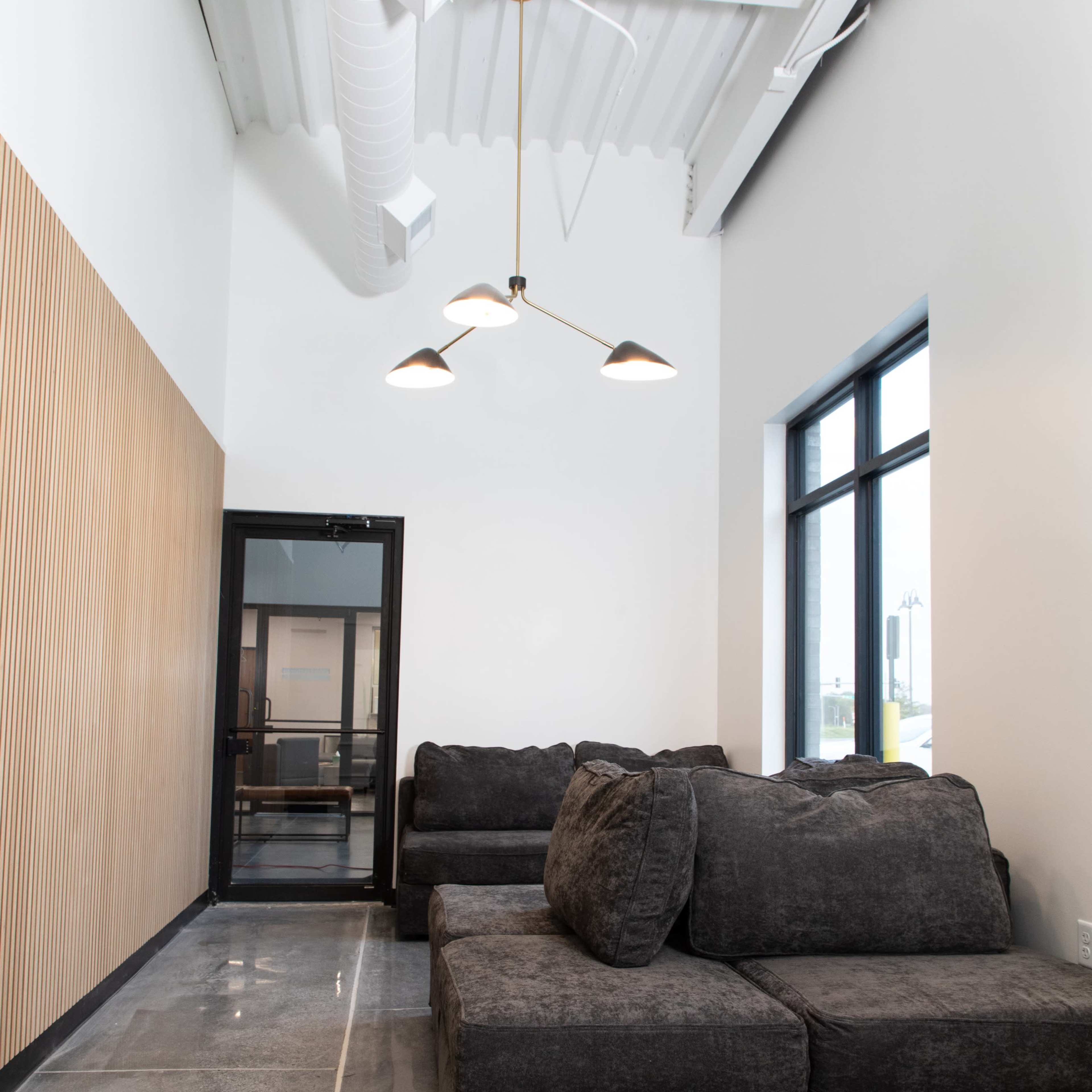 A modern lounge area featuring a dark gray sectional sofa, a large window, and a wooden accent wall.