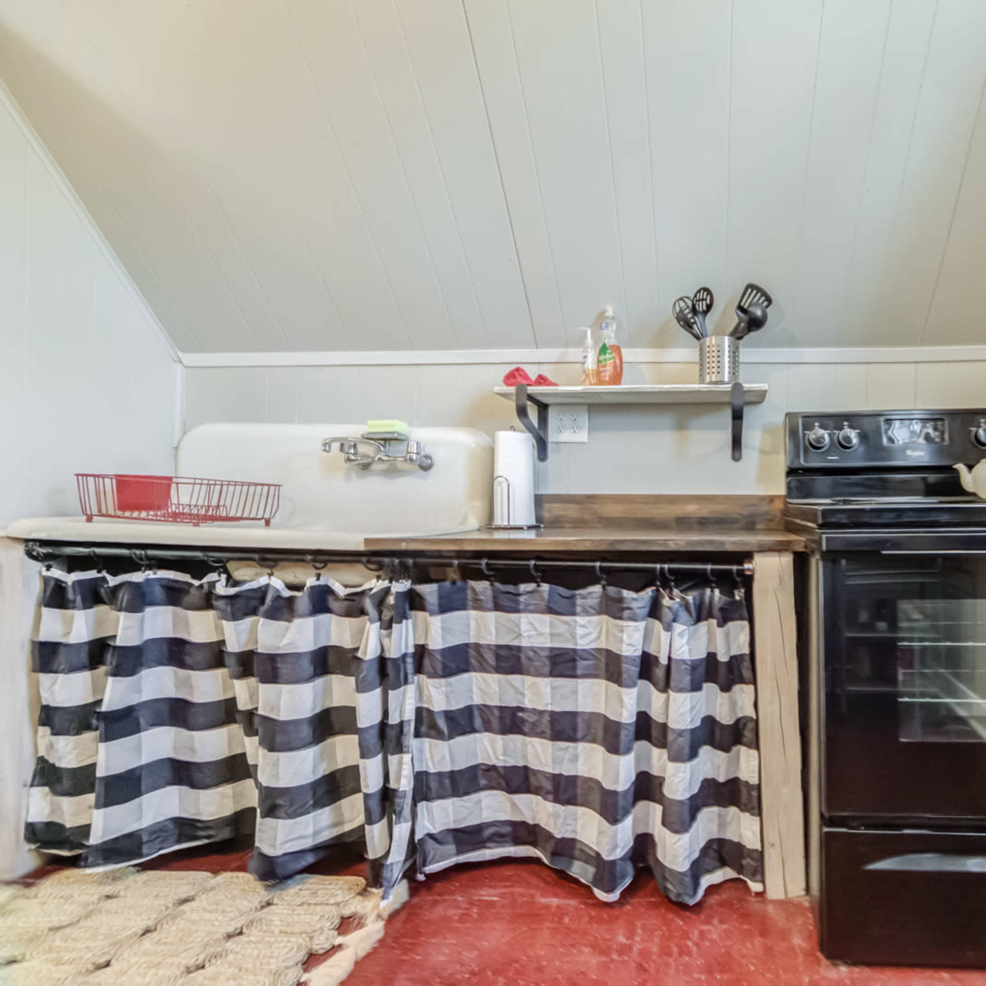 A compact kitchen with a black oven, a sink on the left, and striped curtains covering the space underneath the counter.
