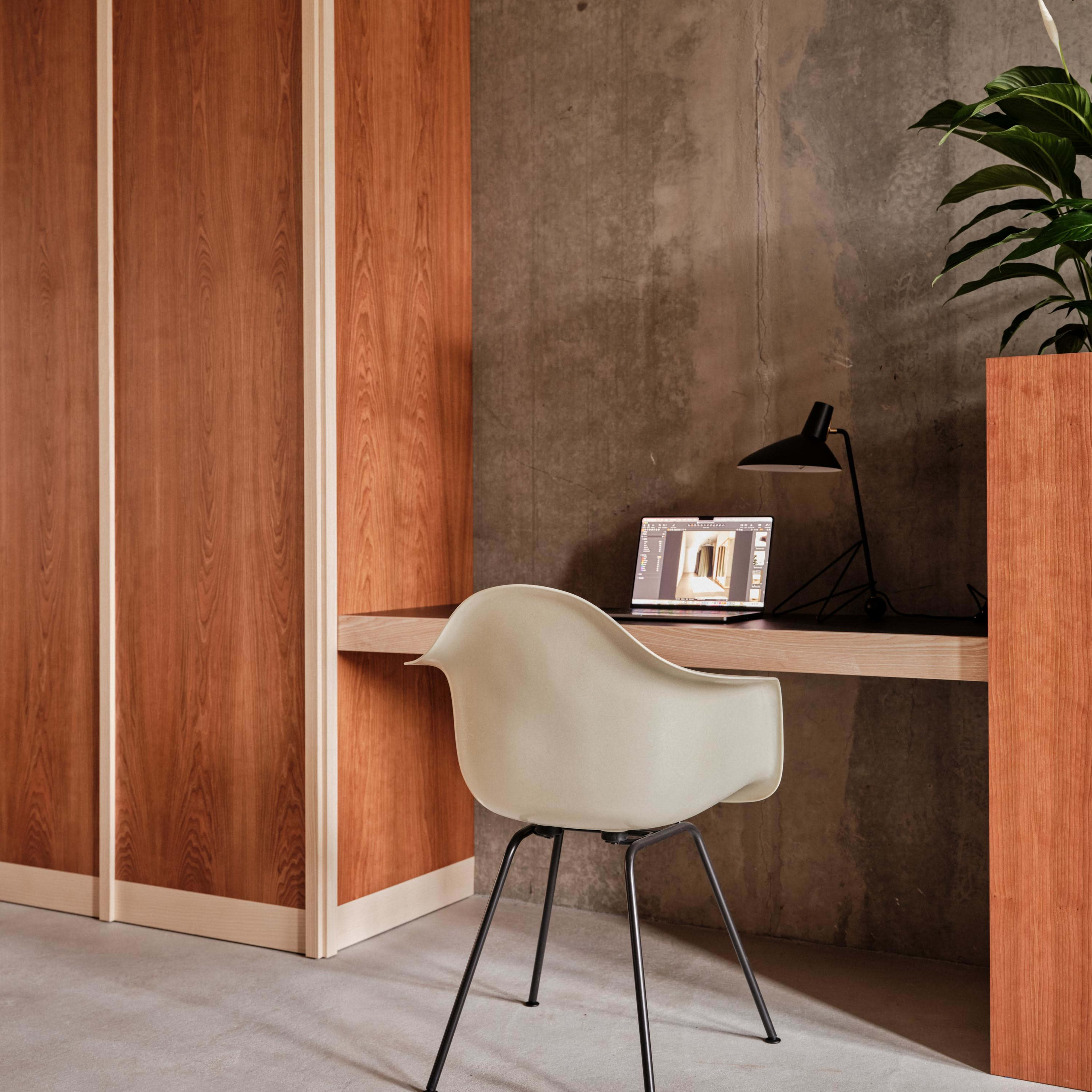 A minimalistic workspace with a chair at a wooden desk, backed by a wooden divider and adorned with a potted plant.