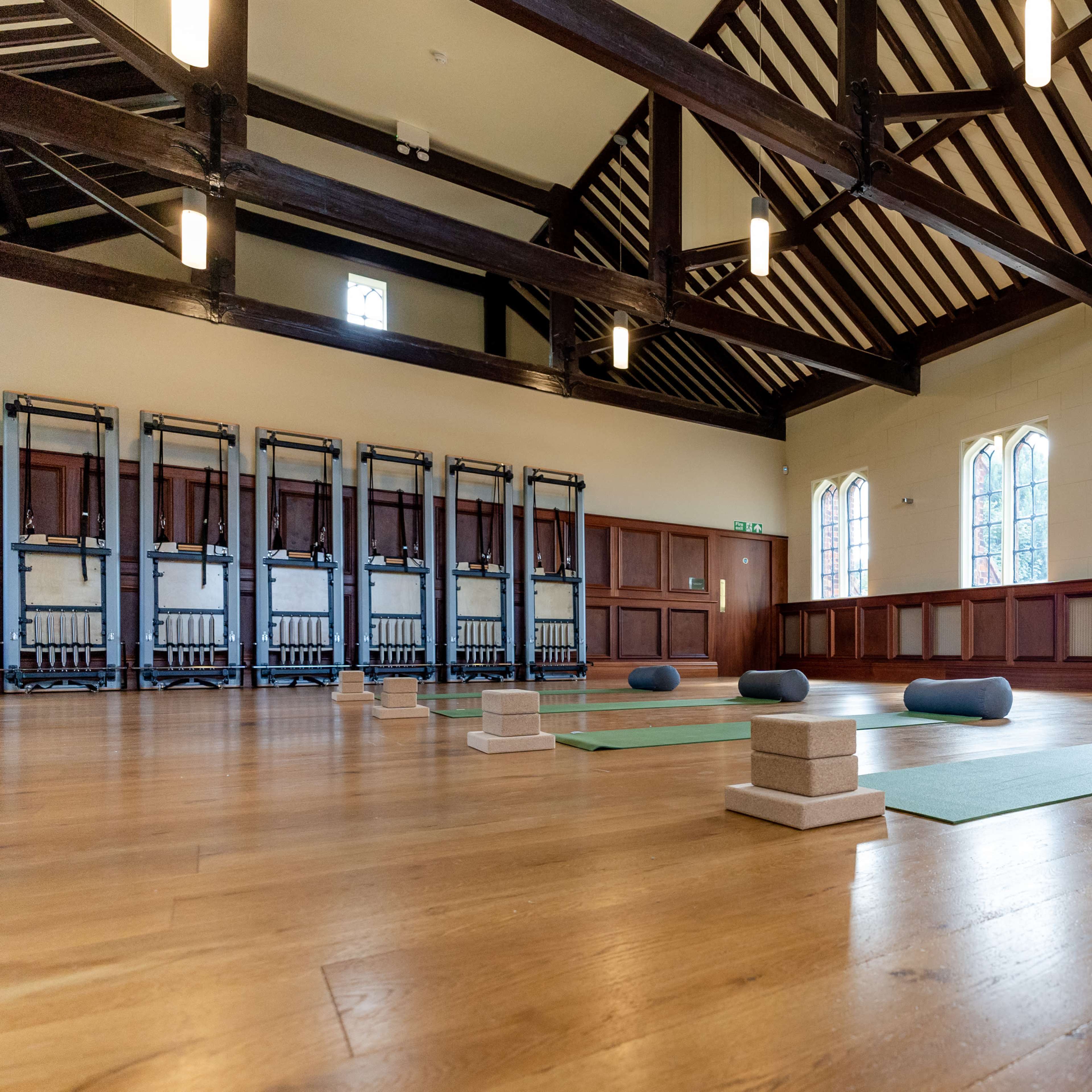 A spacious yoga studio with wooden beams, several yoga mats placed on the wooden floor, and exercise blocks positioned on the mats.