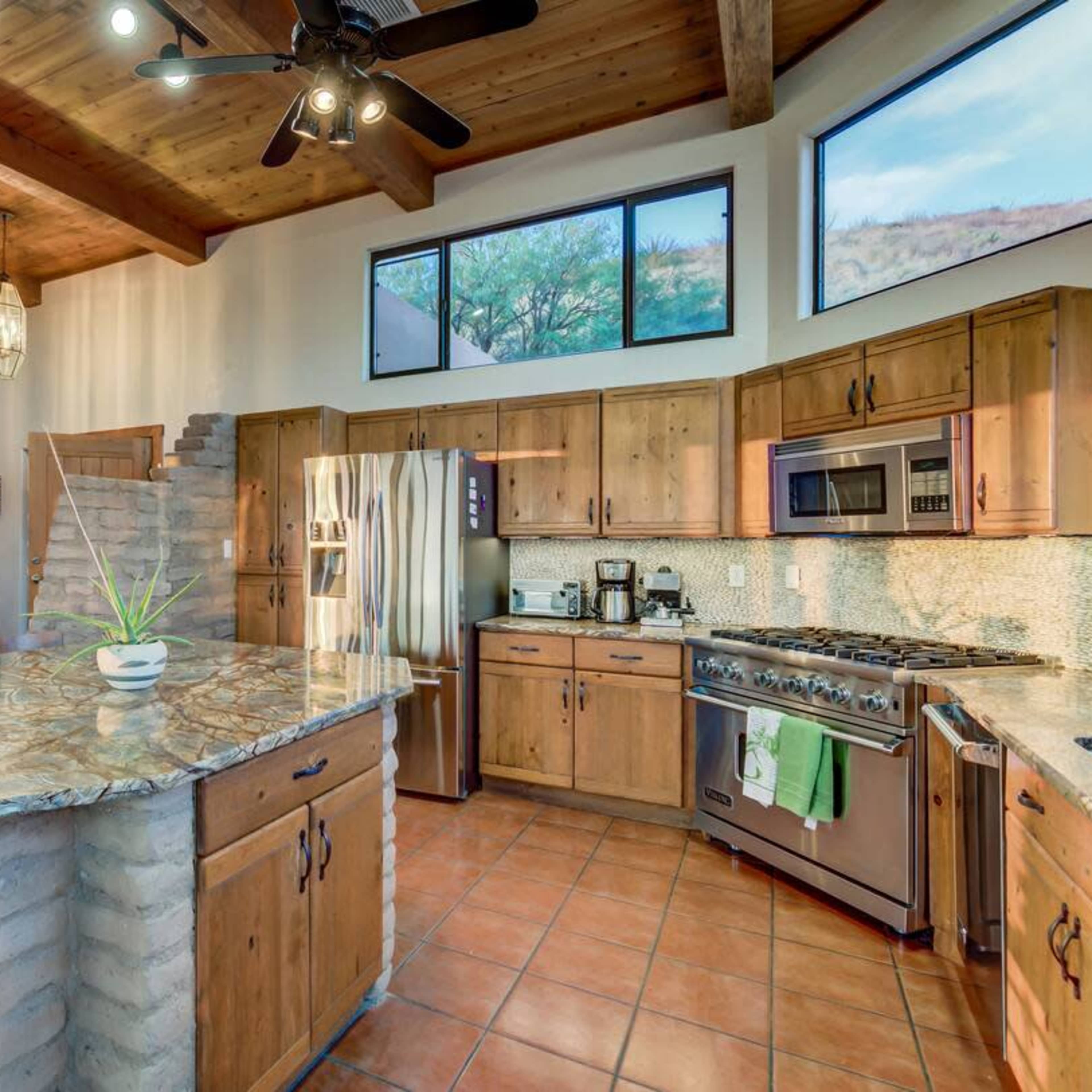 A modern kitchen with wooden cabinets, a large stone island, and an adjacent staircase leading to an upper level.