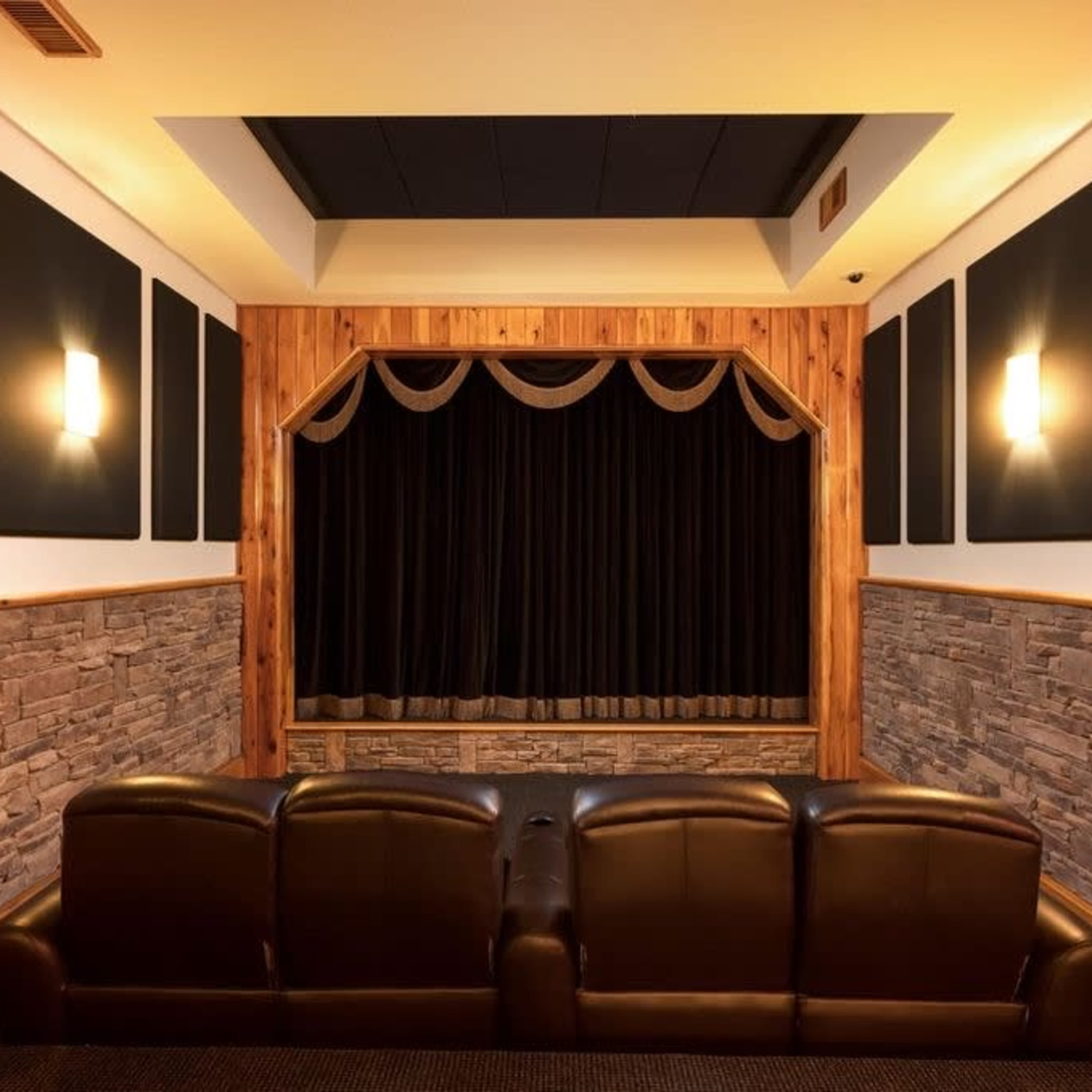 A home theater with a dark curtain stage, wooden wall accents, and a pair of brown leather recliners facing the screen.
