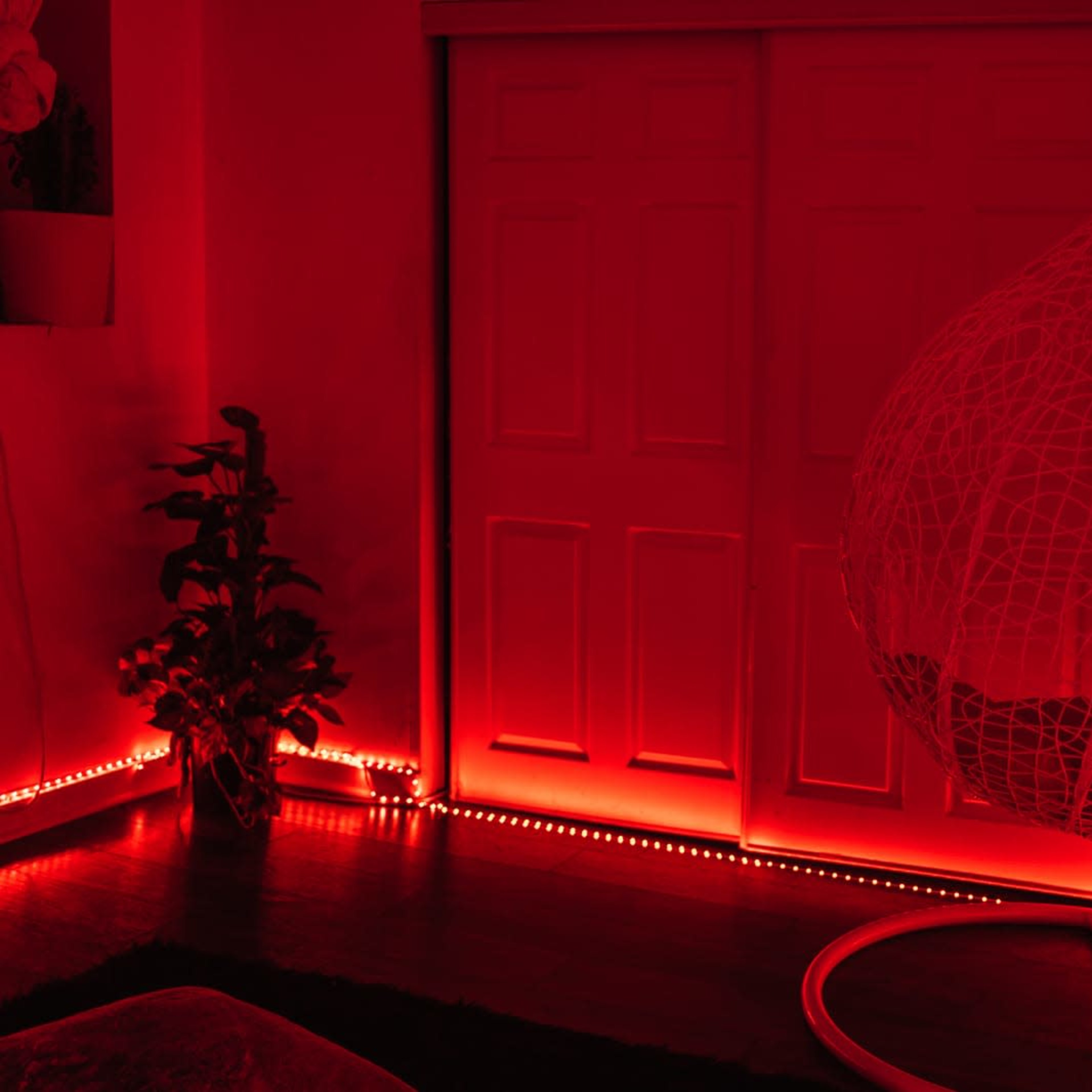 A hanging chair is positioned beside a plant, with red LED lights illuminating the room's walls and floor.