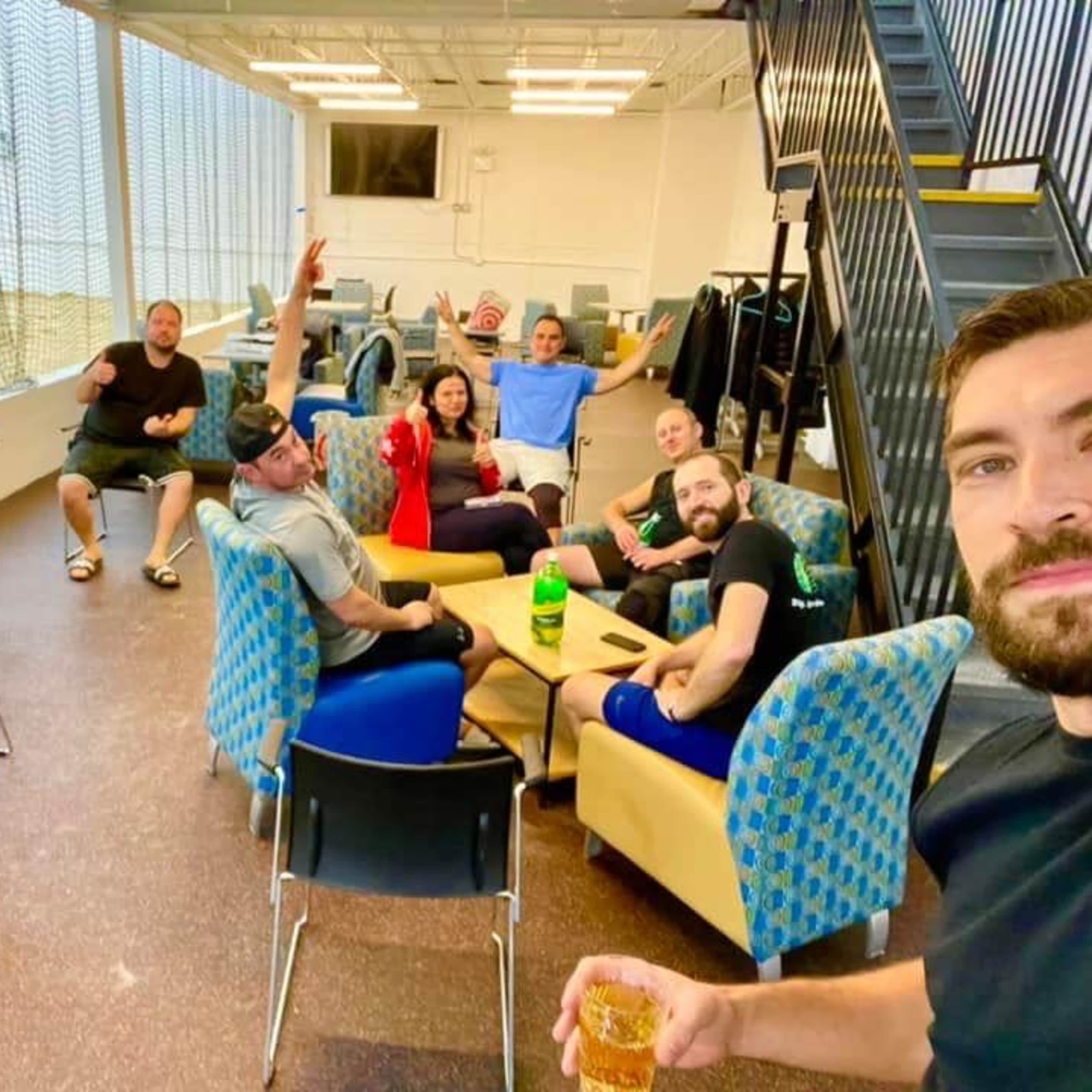 A group of people is gathered in a lounge area, sitting and standing in various poses while engaging with one another.