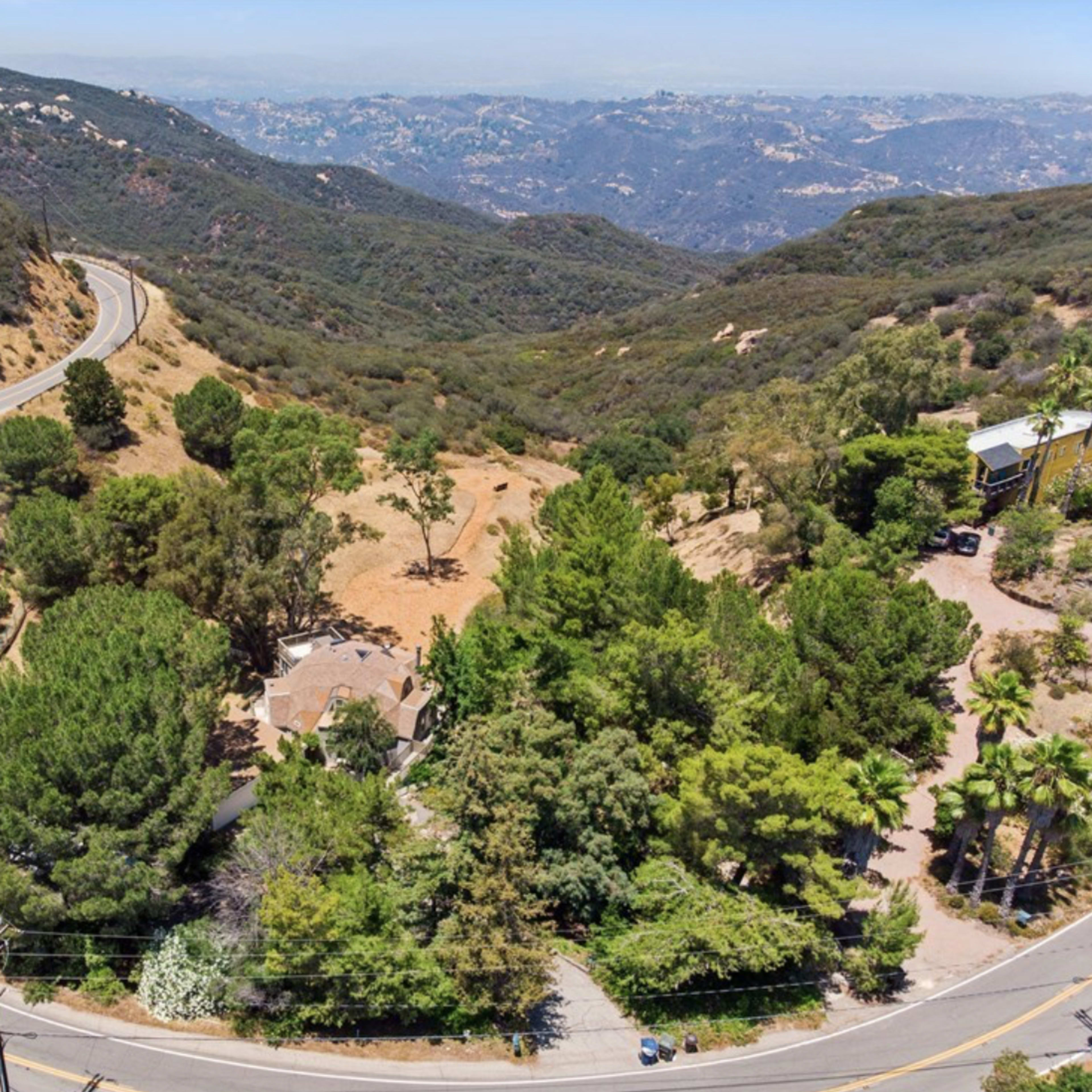 A winding road curving through a mountainous landscape with sparse trees and a few buildings nestled among the hills.