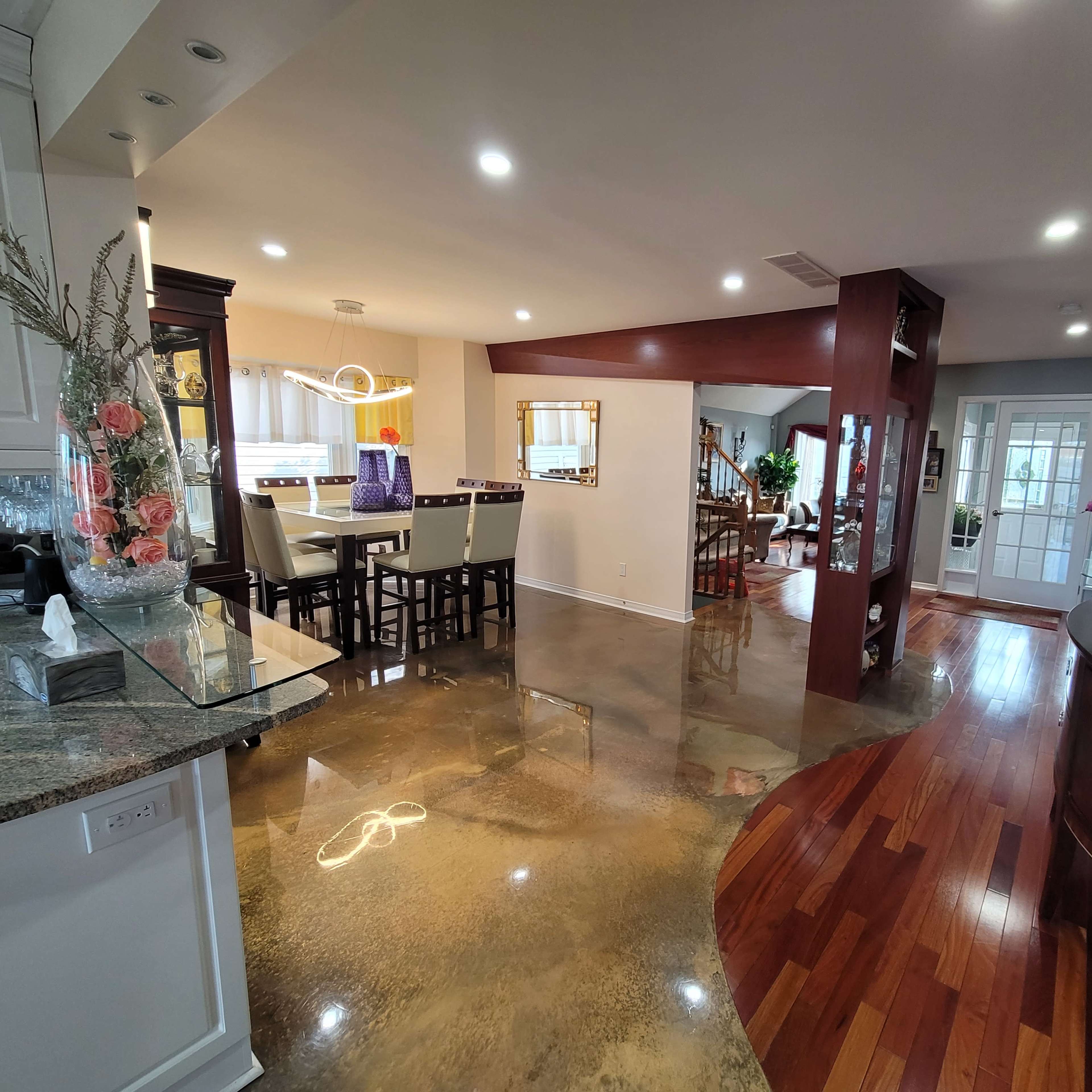 A modern open-concept living space featuring a kitchen with a breakfast bar, a dining area, and a hallway leading to a staircase.