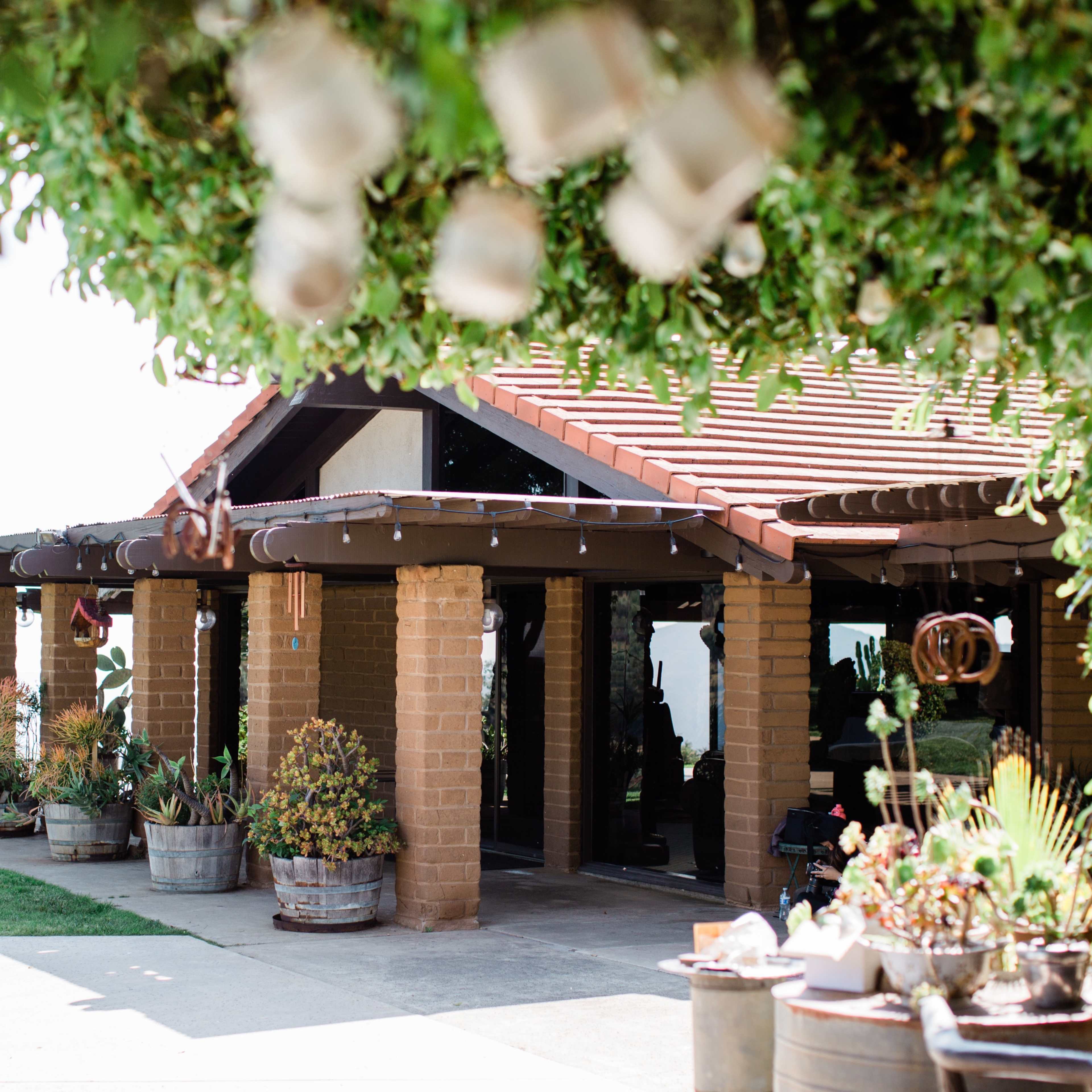 A rustic building with a red-tiled roof, surrounded by potted plants and hanging lanterns.
