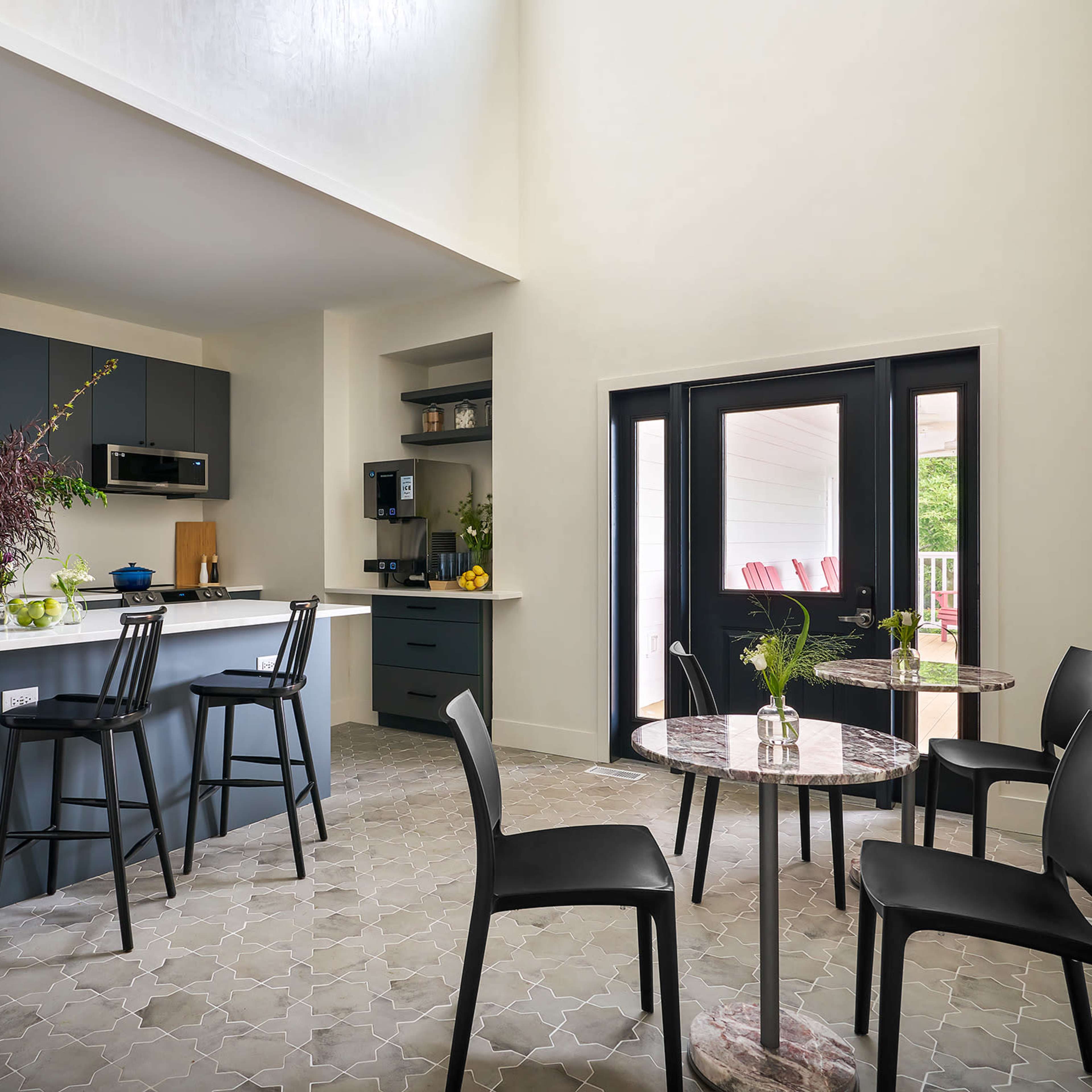 A modern kitchen features dark cabinetry and a dining area with black chairs around a marble-topped table.
