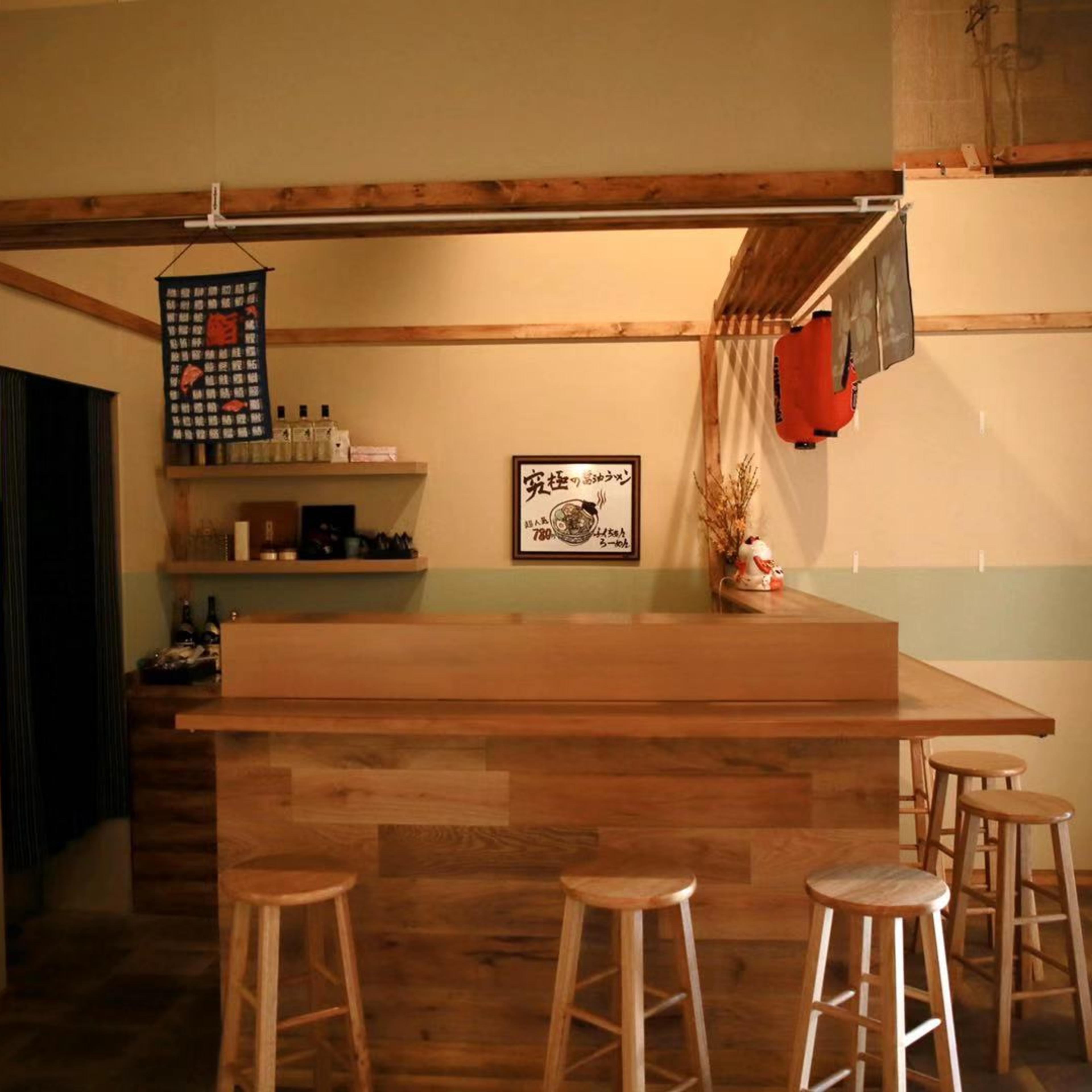 A wooden bar with four stools is set against a wall adorned with minimalist decor in a softly lit room.