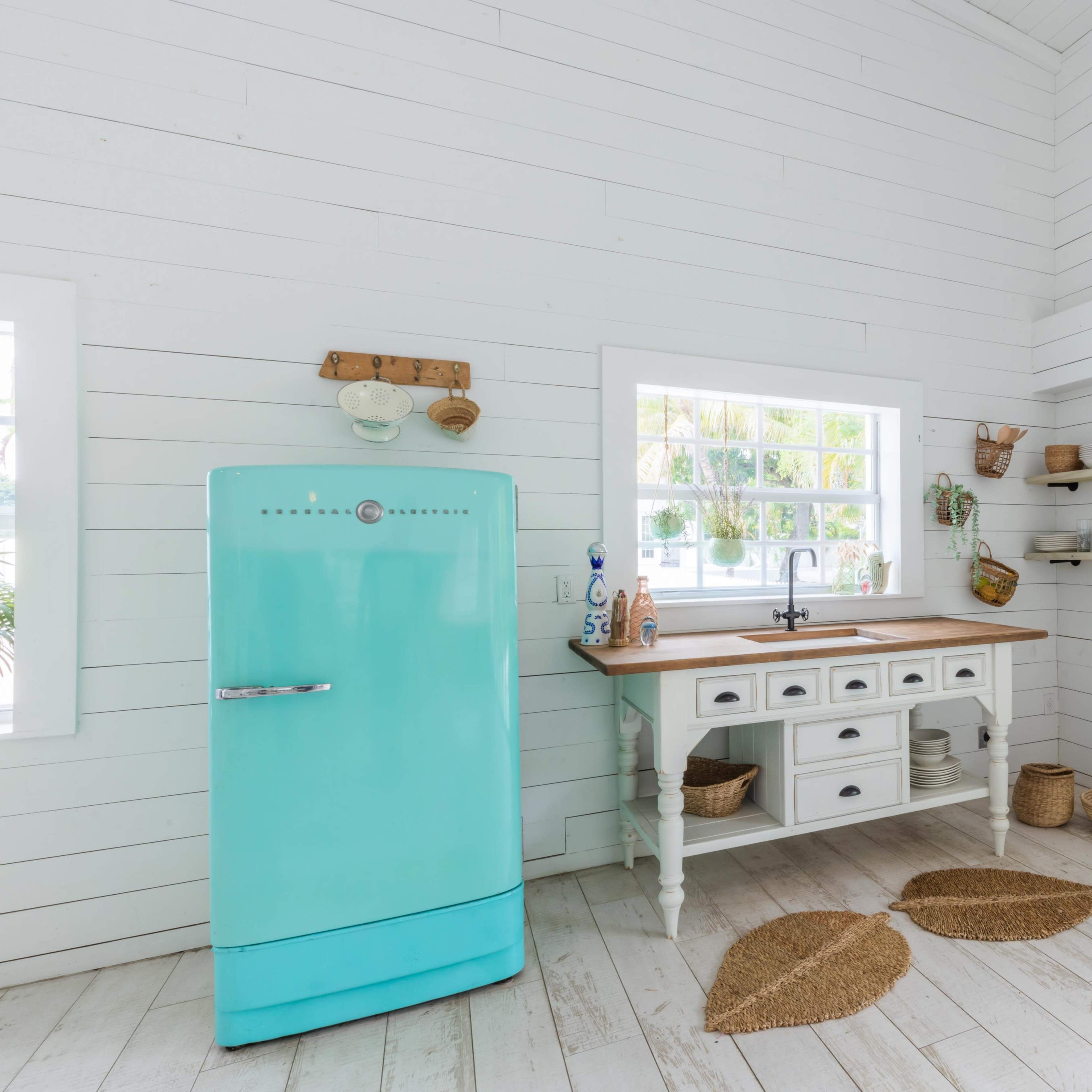 The kitchen features a vintage turquoise refrigerator beside a wooden countertop with drawers, set against white shiplap walls and natural woven decor.