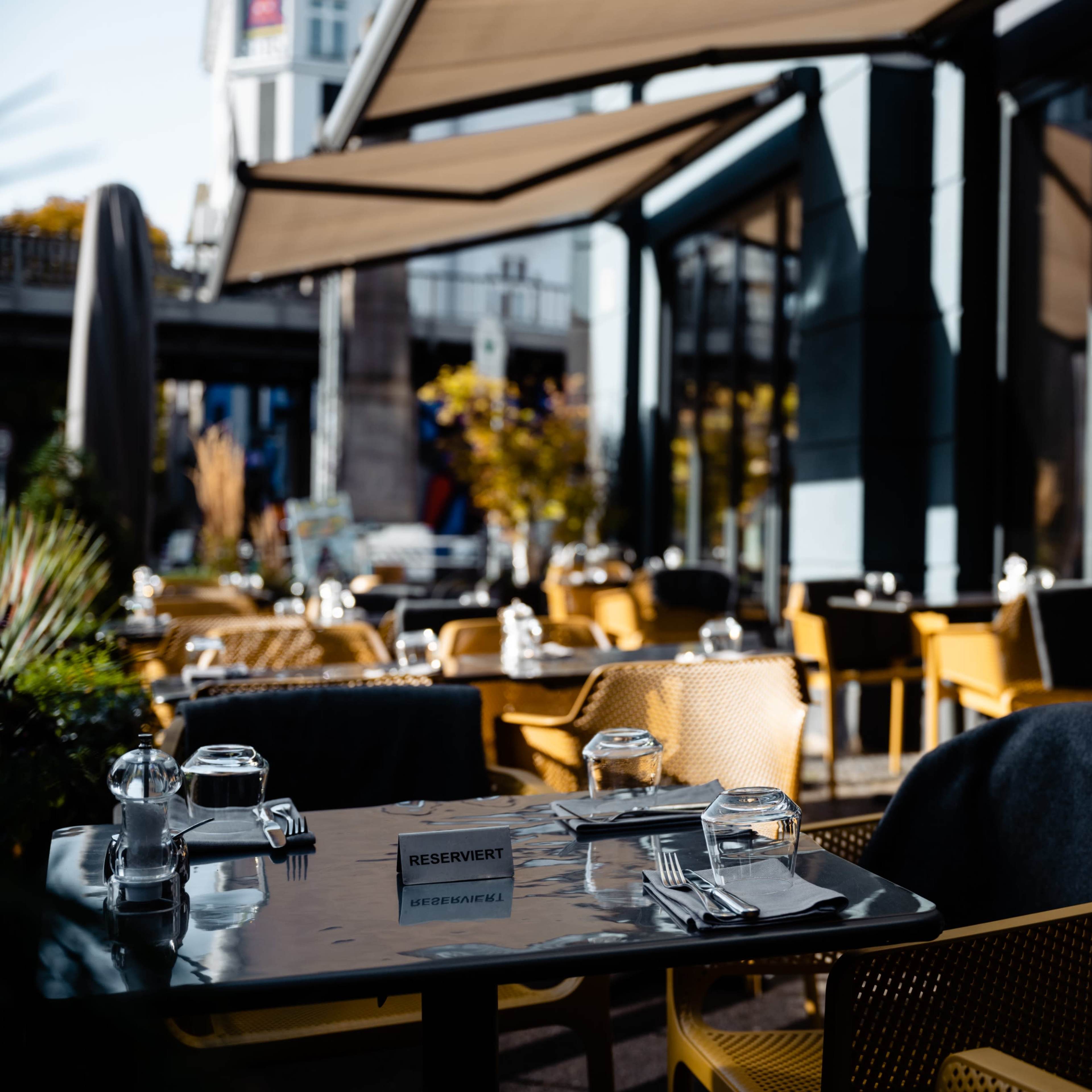 A restaurant patio features neatly set tables with reserved signs, surrounded by golden autumn foliage.