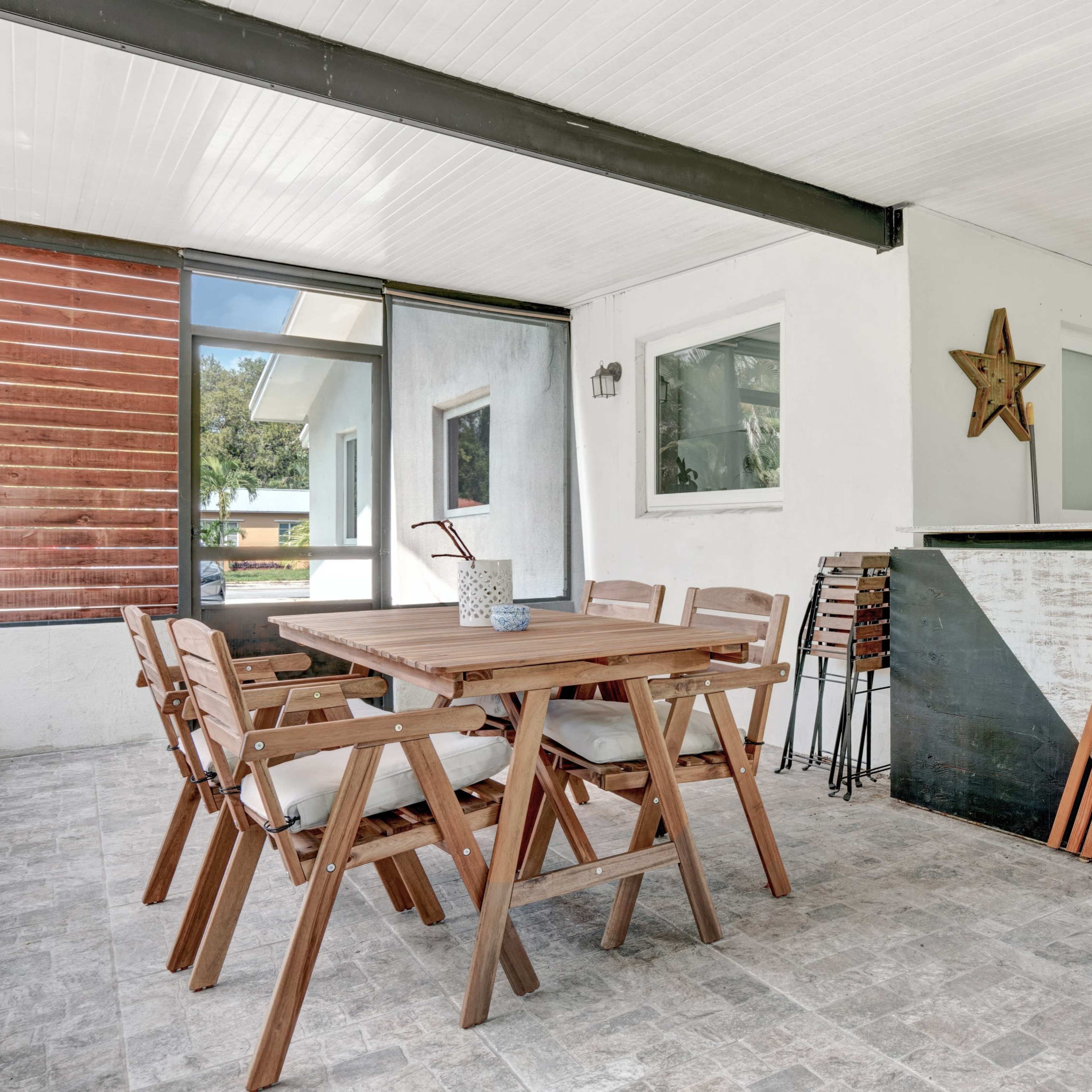 A covered outdoor seating area with a wooden dining table and chairs beside a small bar counter.