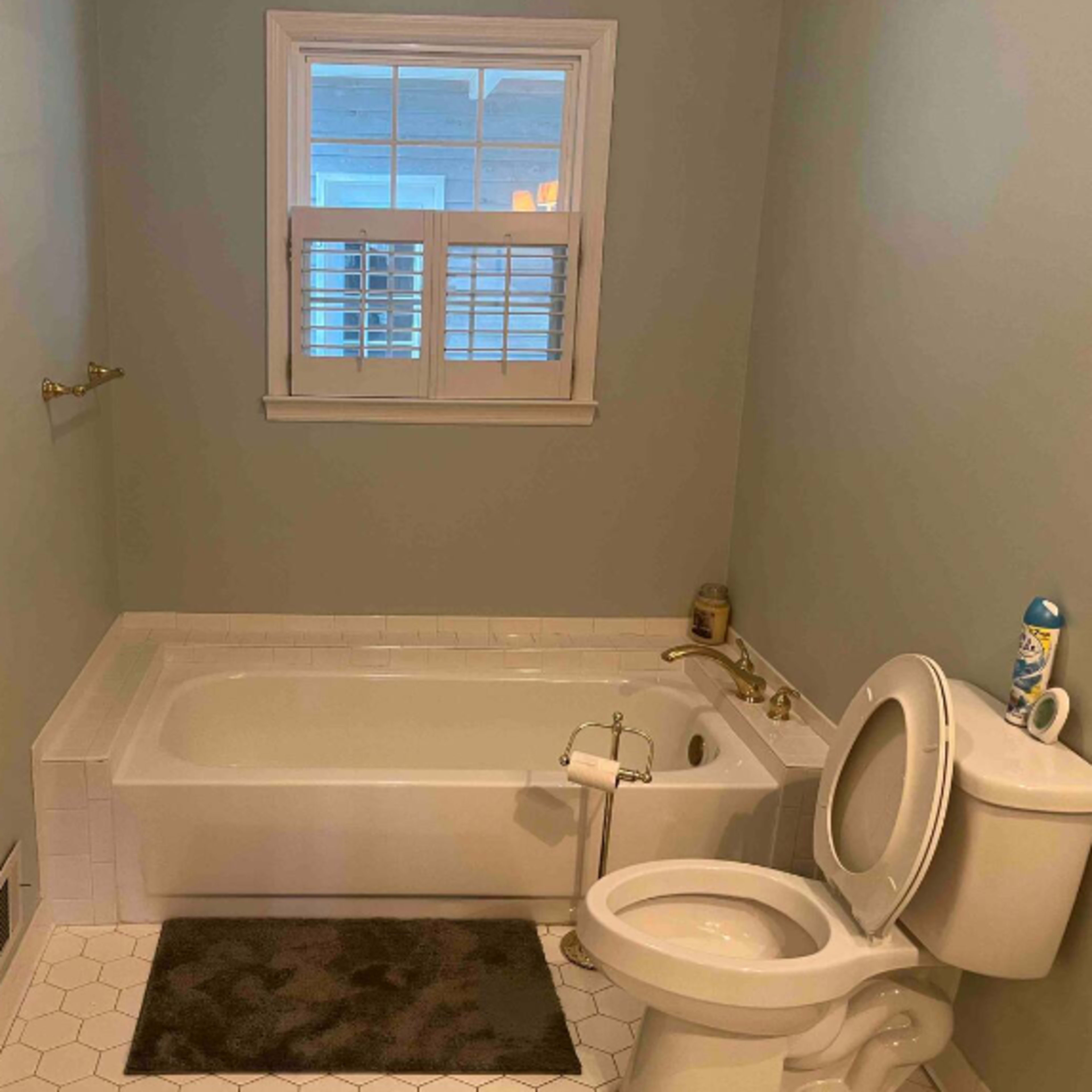 A bathroom featuring a bathtub, a toilet, and a window with blinds.
