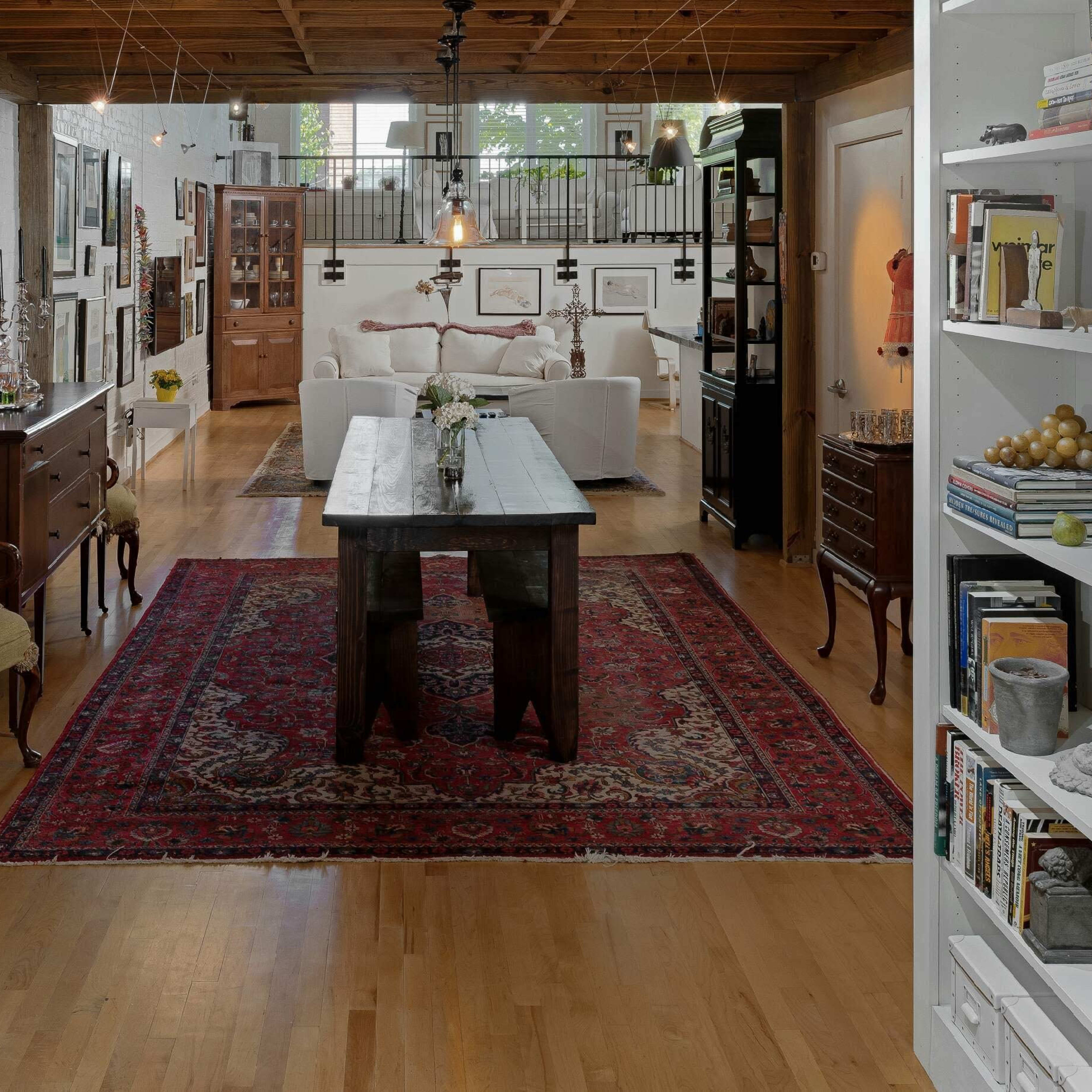 A spacious, open-concept living area with wooden beams, a large rug, and a seating area featuring white sofas.