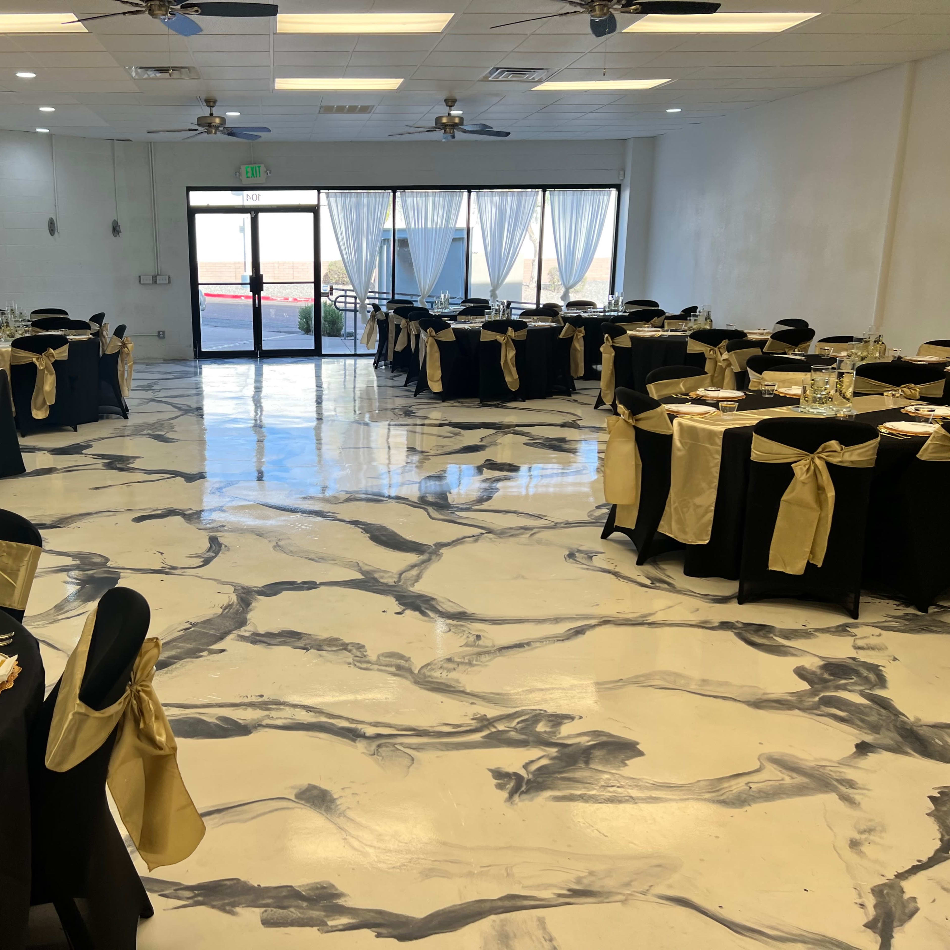 A banquet hall with tables set for an event, featuring black tablecloths, gold accents, and a polished marble-like floor.
