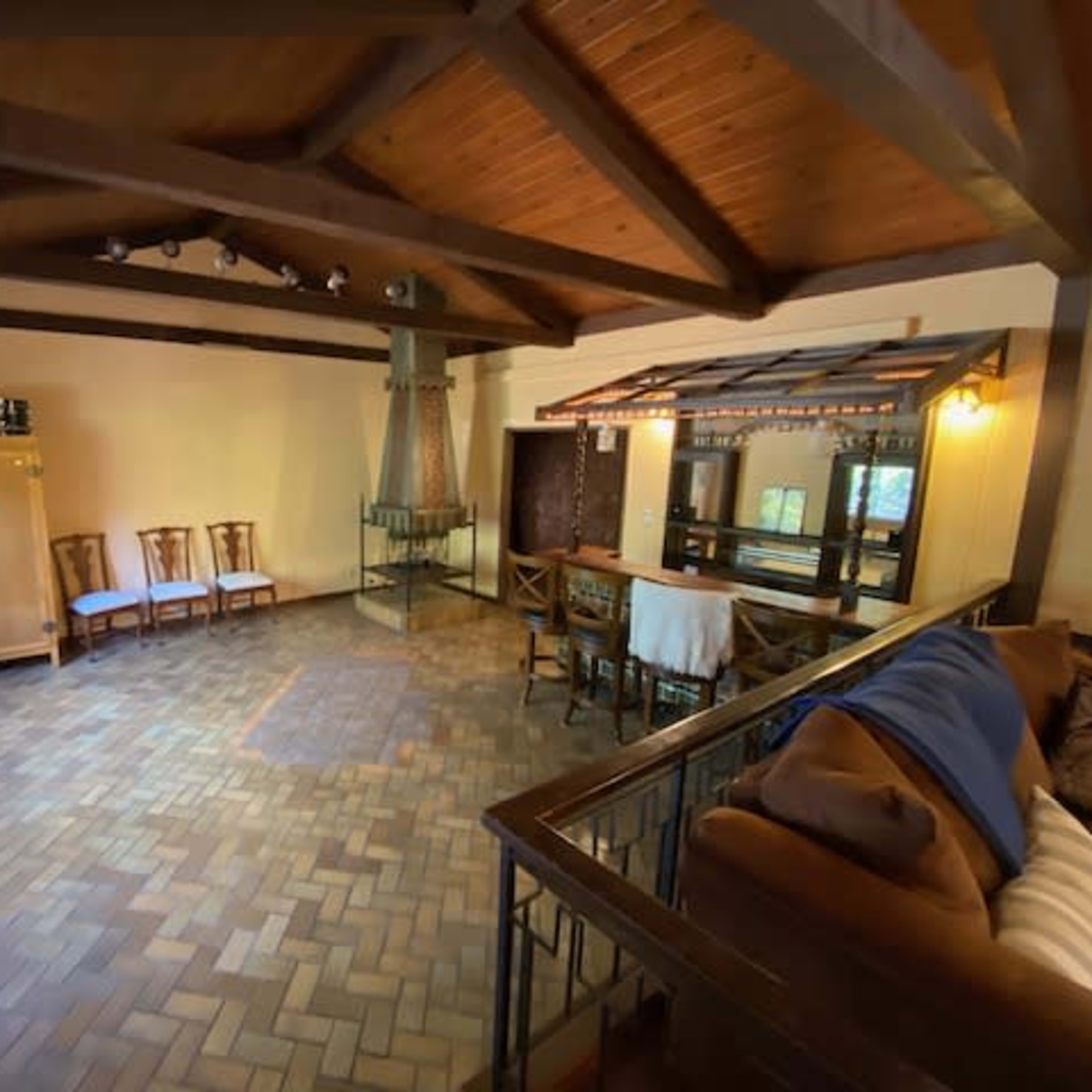 A spacious room with wooden beams, tiled flooring, and a mix of seating arrangements along with a bar area.