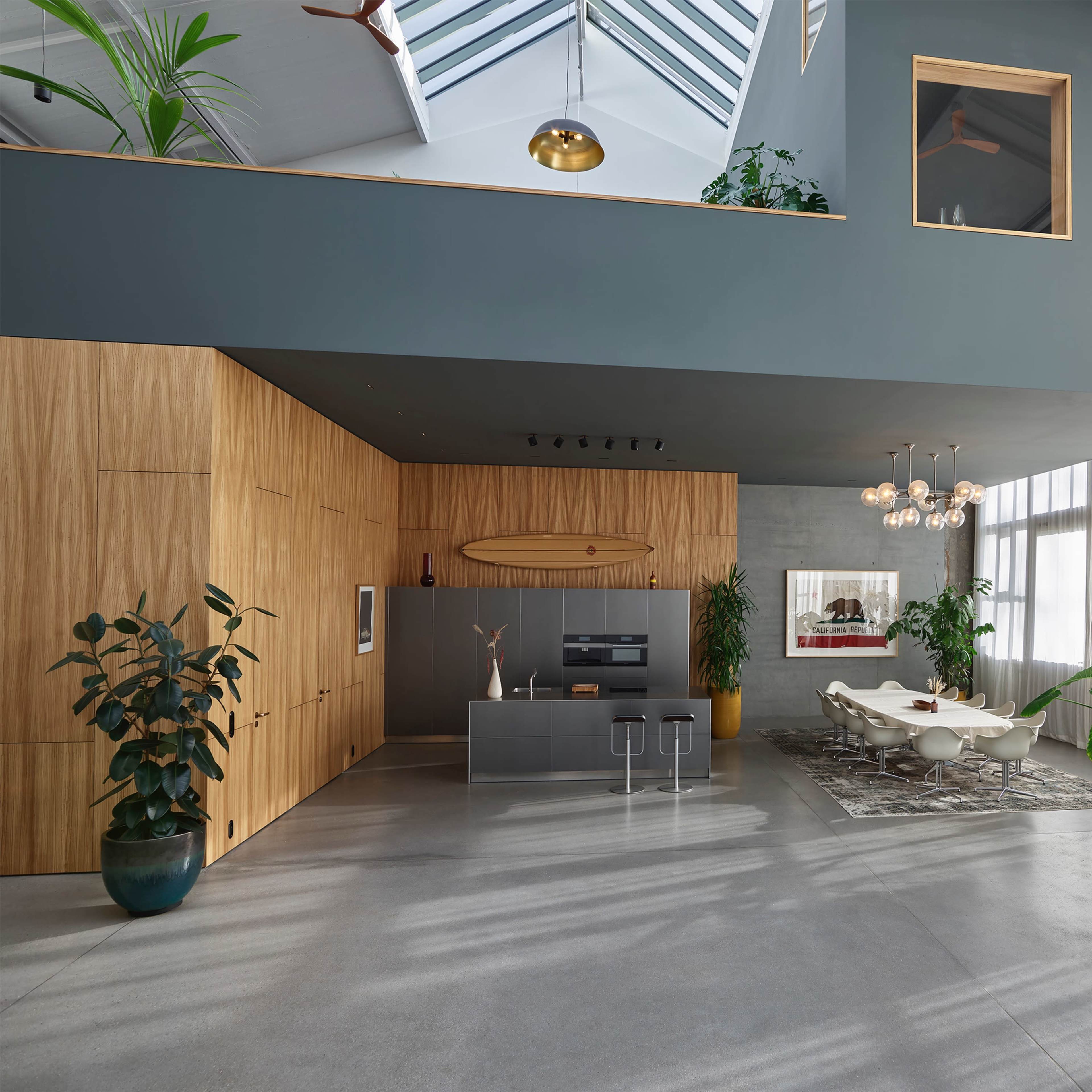 A modern, open-concept living area with a kitchen island, large windows, and indoor plants.