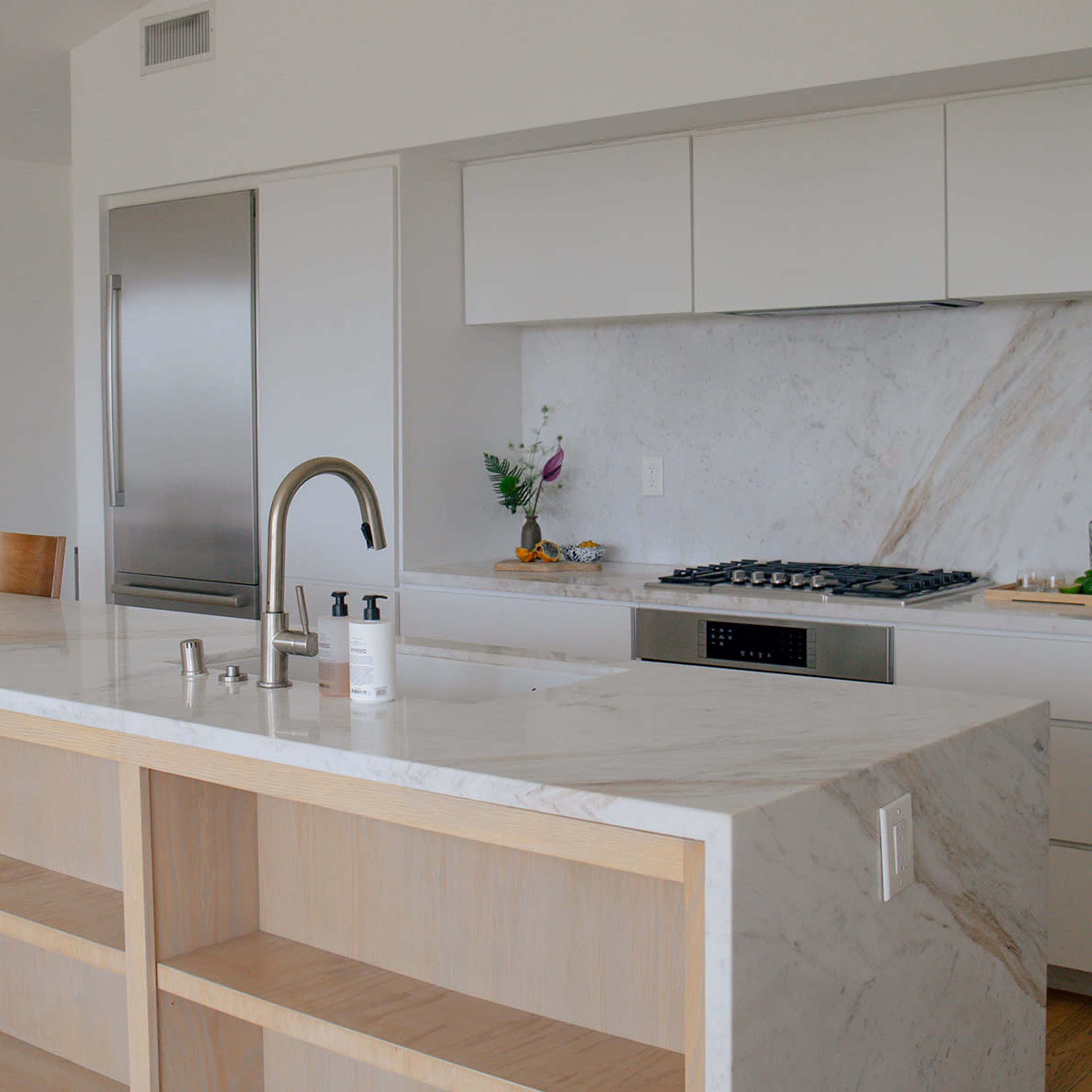 A modern kitchen featuring a marble countertop, a sleek stove, and minimalist cabinetry, with a dining space in the background.