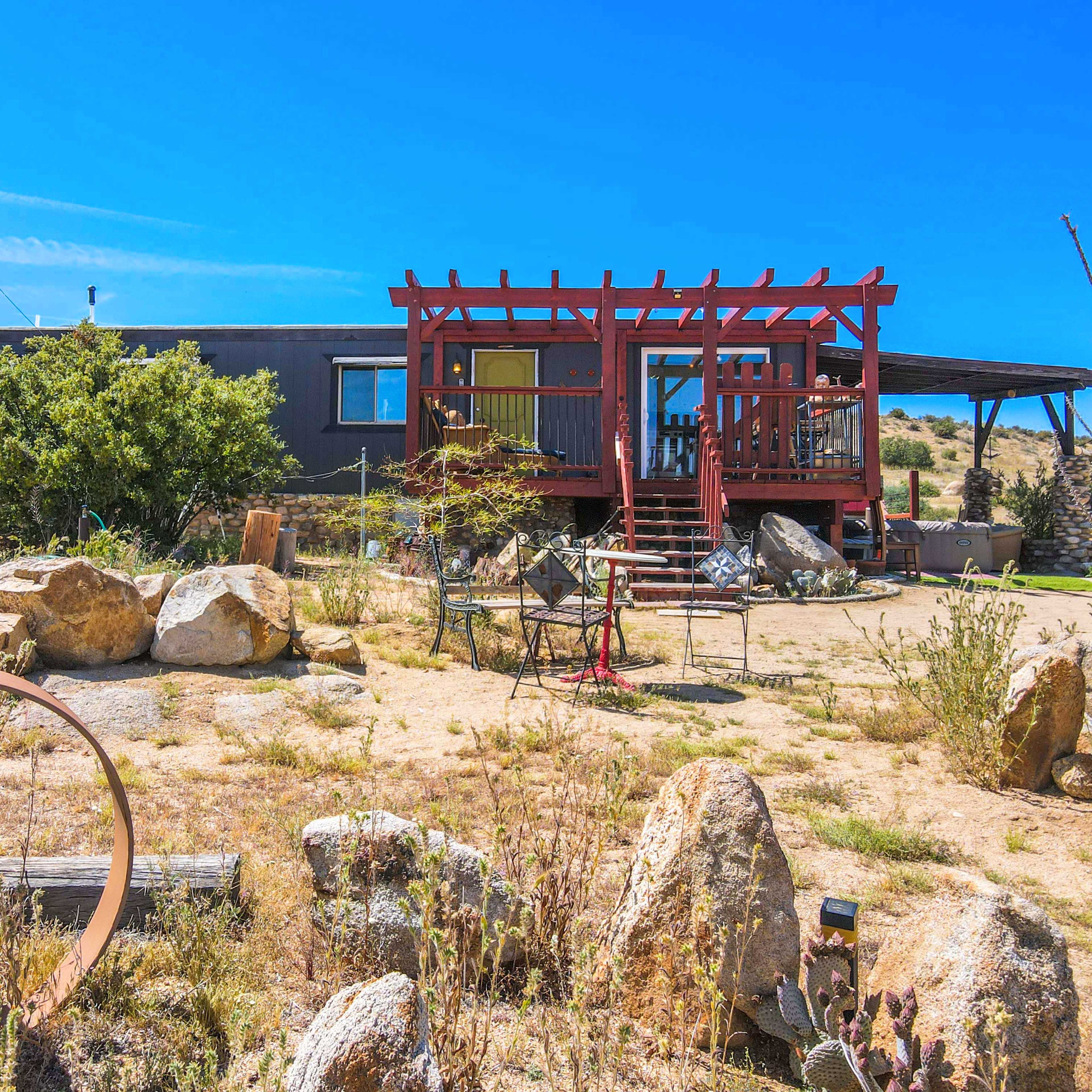 A modern house with a red pergola and a wooden deck sits amidst rocky terrain and sparse vegetation.