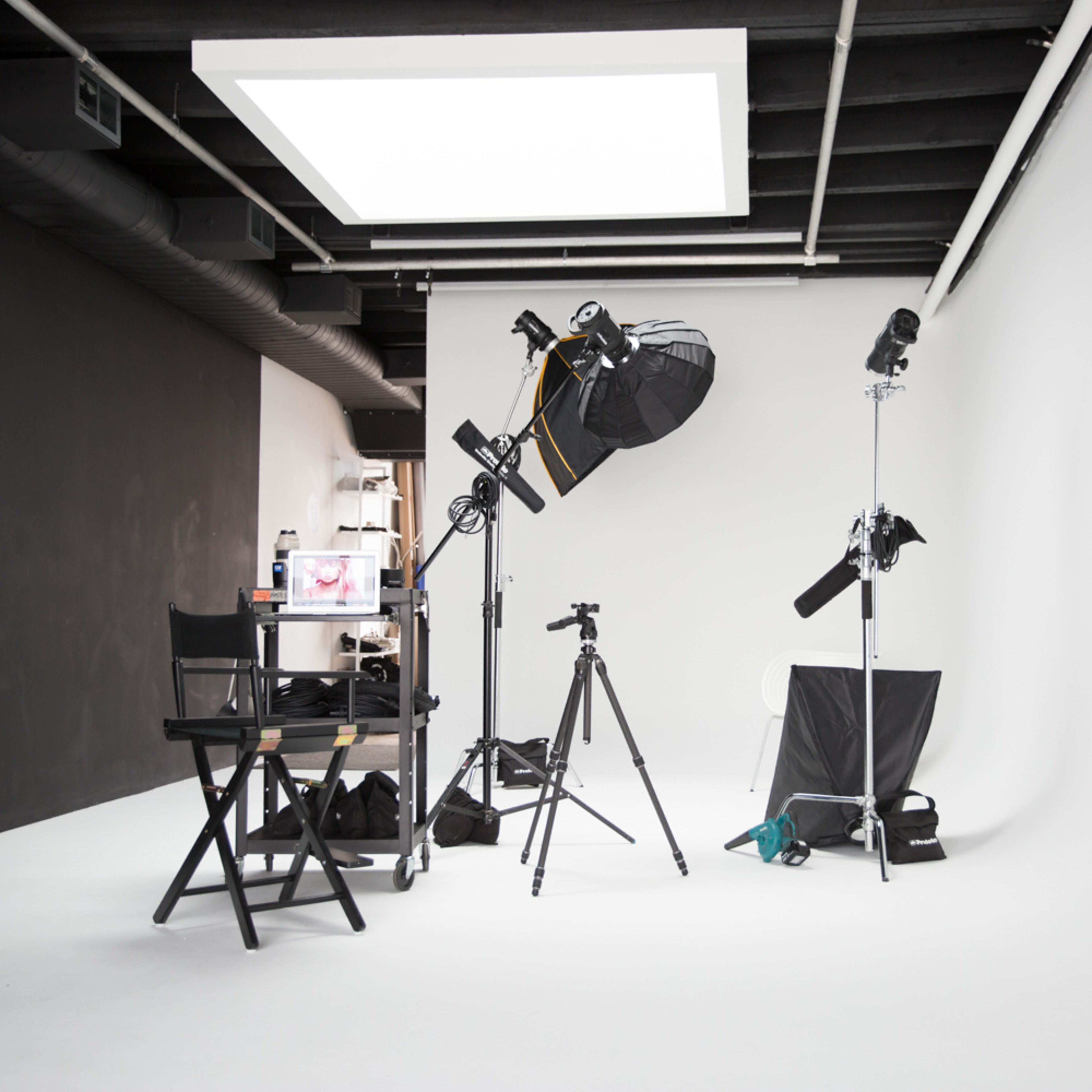 A photography studio equipped with lighting gear, tripods, a director's chair, and a blank backdrop.