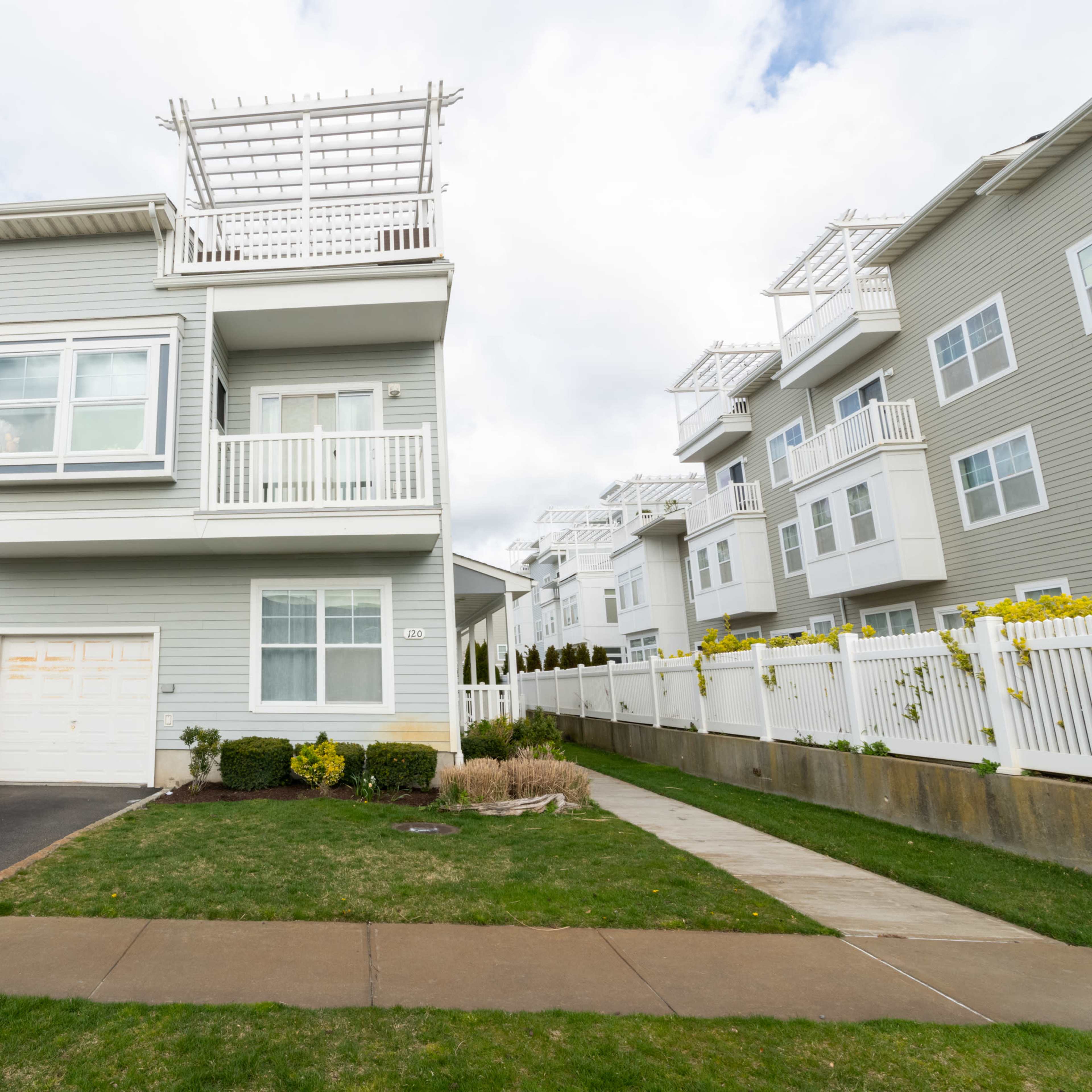 A modern two-story residential building with balconies and a garage is situated beside a paved driveway and grassy lawn.