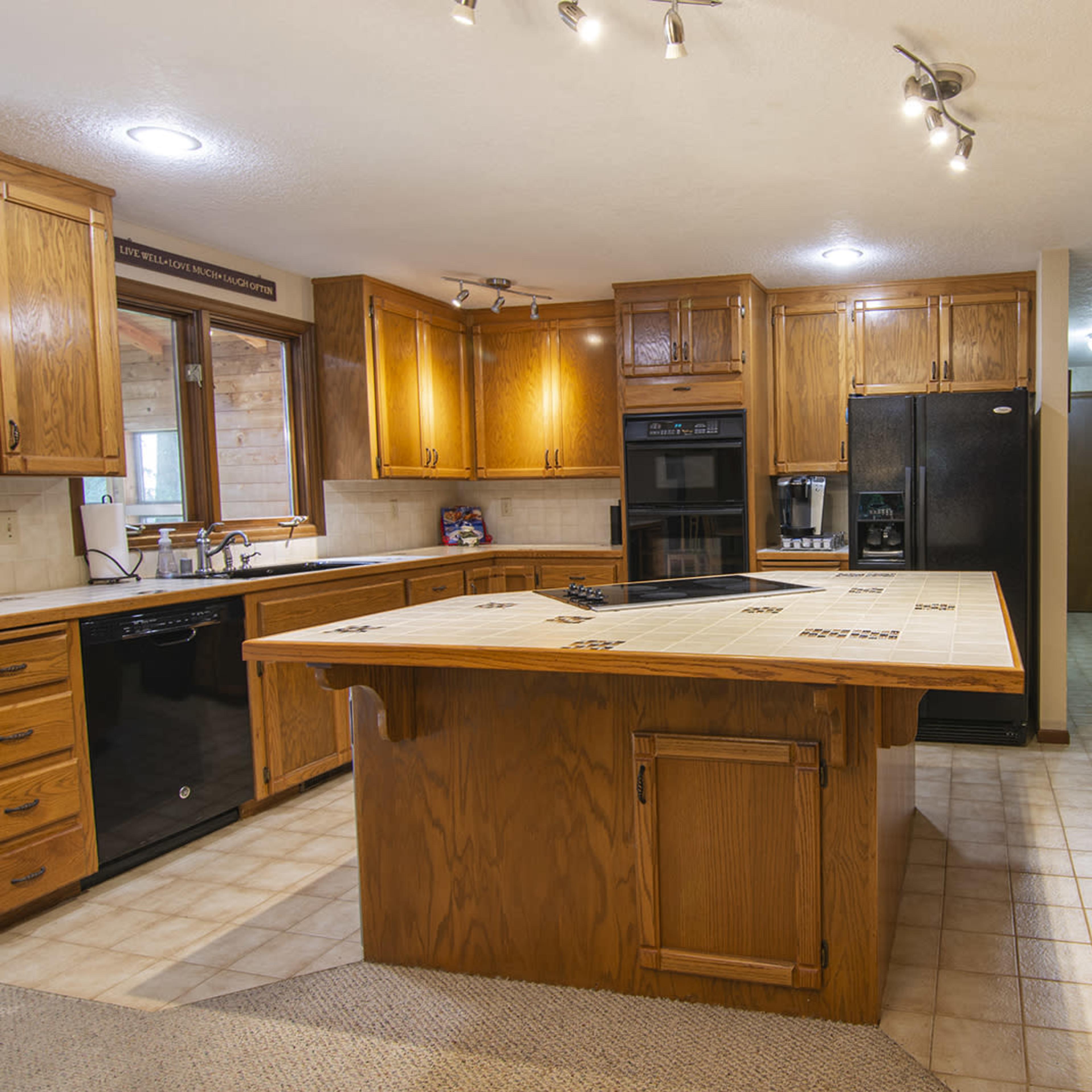 A spacious kitchen with wooden cabinets, a central island with a tile countertop, and black appliances.