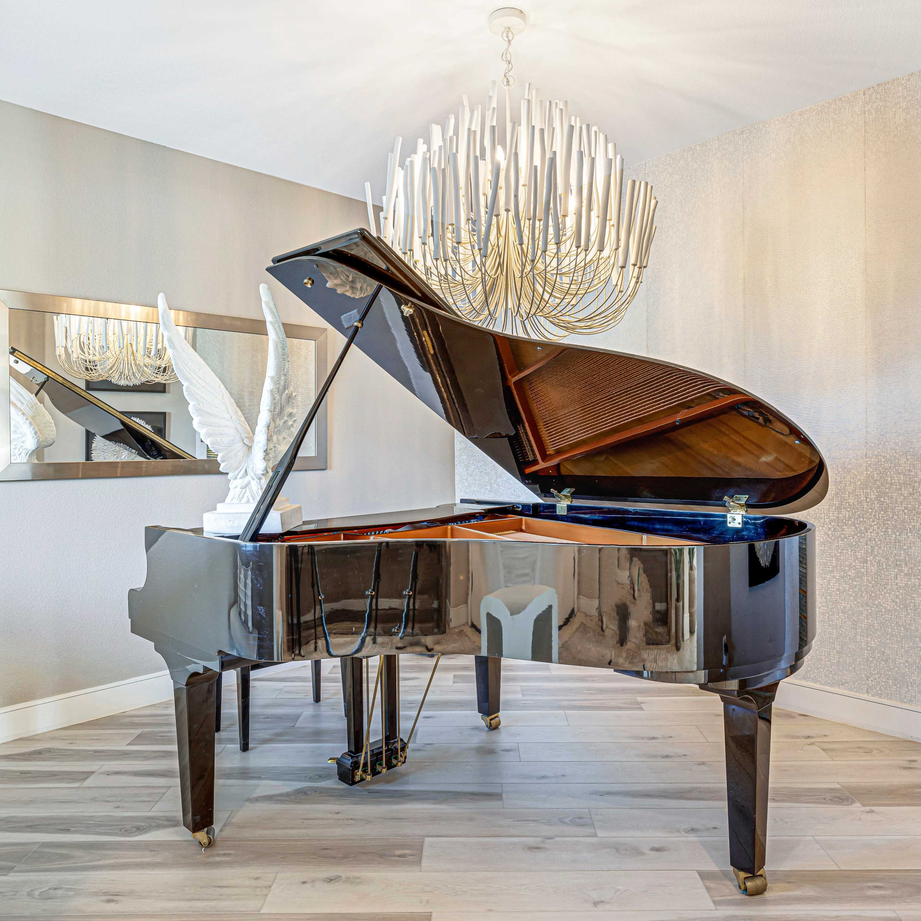 A grand piano with a decorative sculpture sits in a well-lit room featuring a modern chandelier and a mirrored wall.
