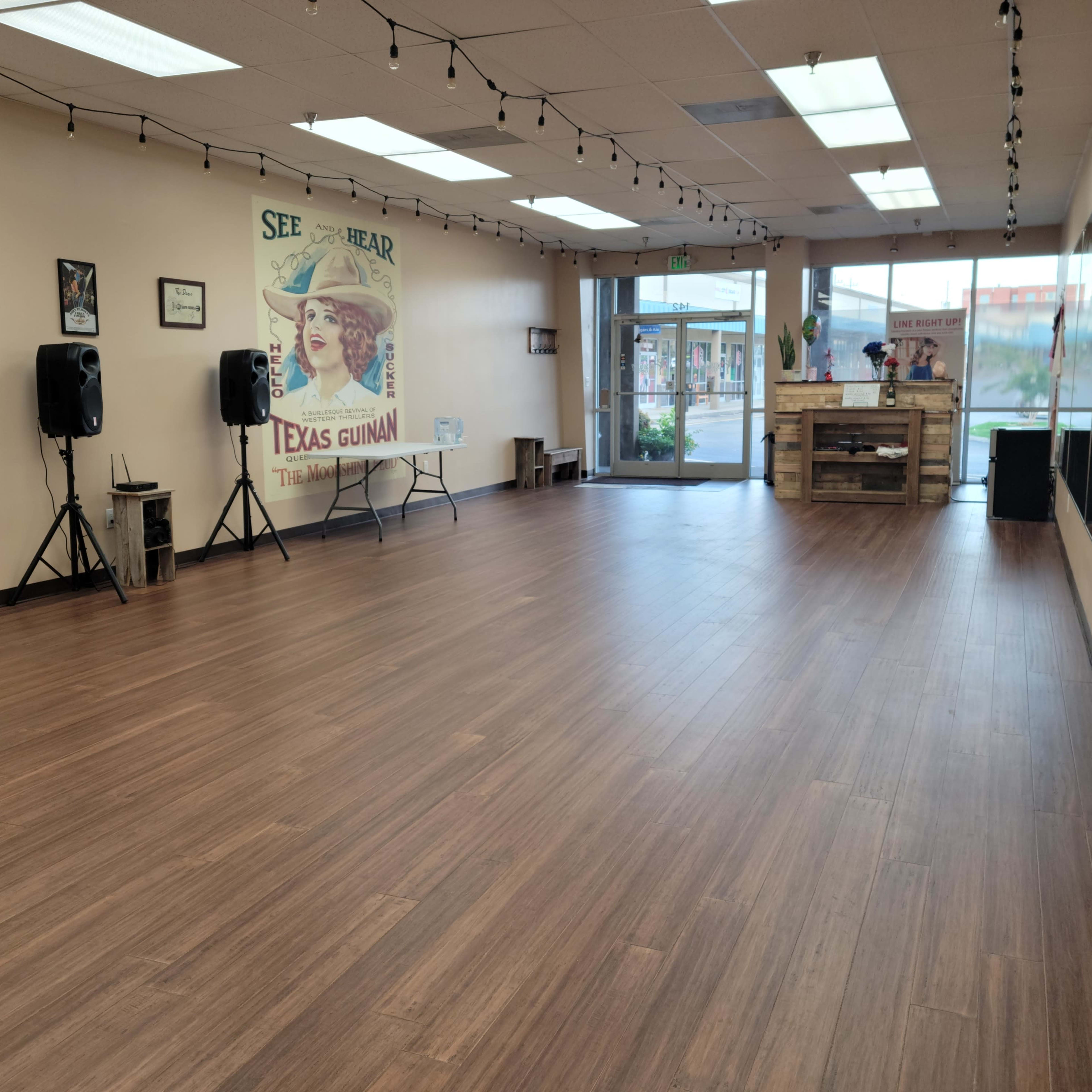 A spacious, empty studio with wooden flooring, featuring a large window at one end and a poster on the wall.