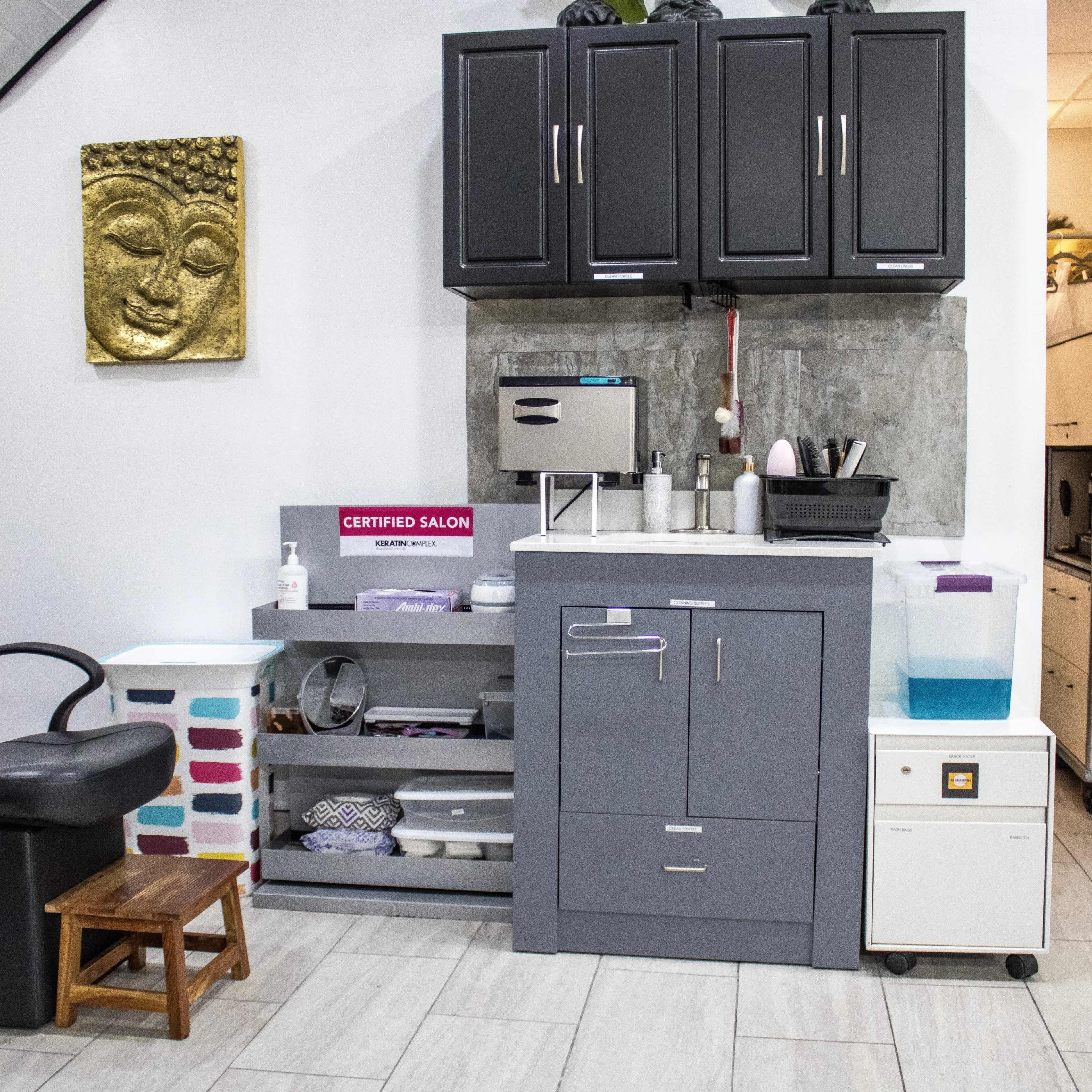 The interior of a salon featuring a black chair, storage cabinets, a sink area, and decorative elements on the walls.