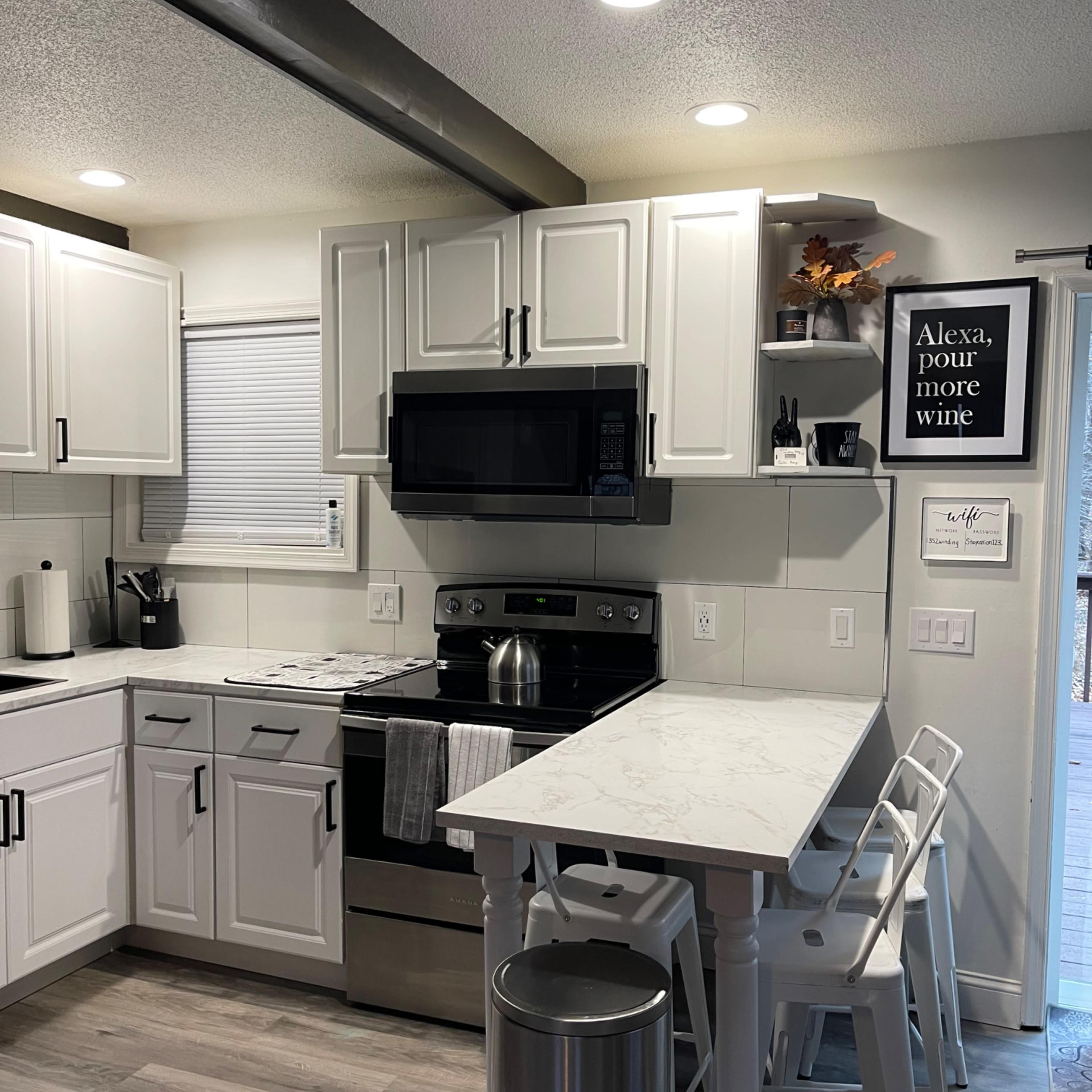 The kitchen features white cabinets, a stainless steel refrigerator and microwave, a marble countertop, and a small dining area with three stools.