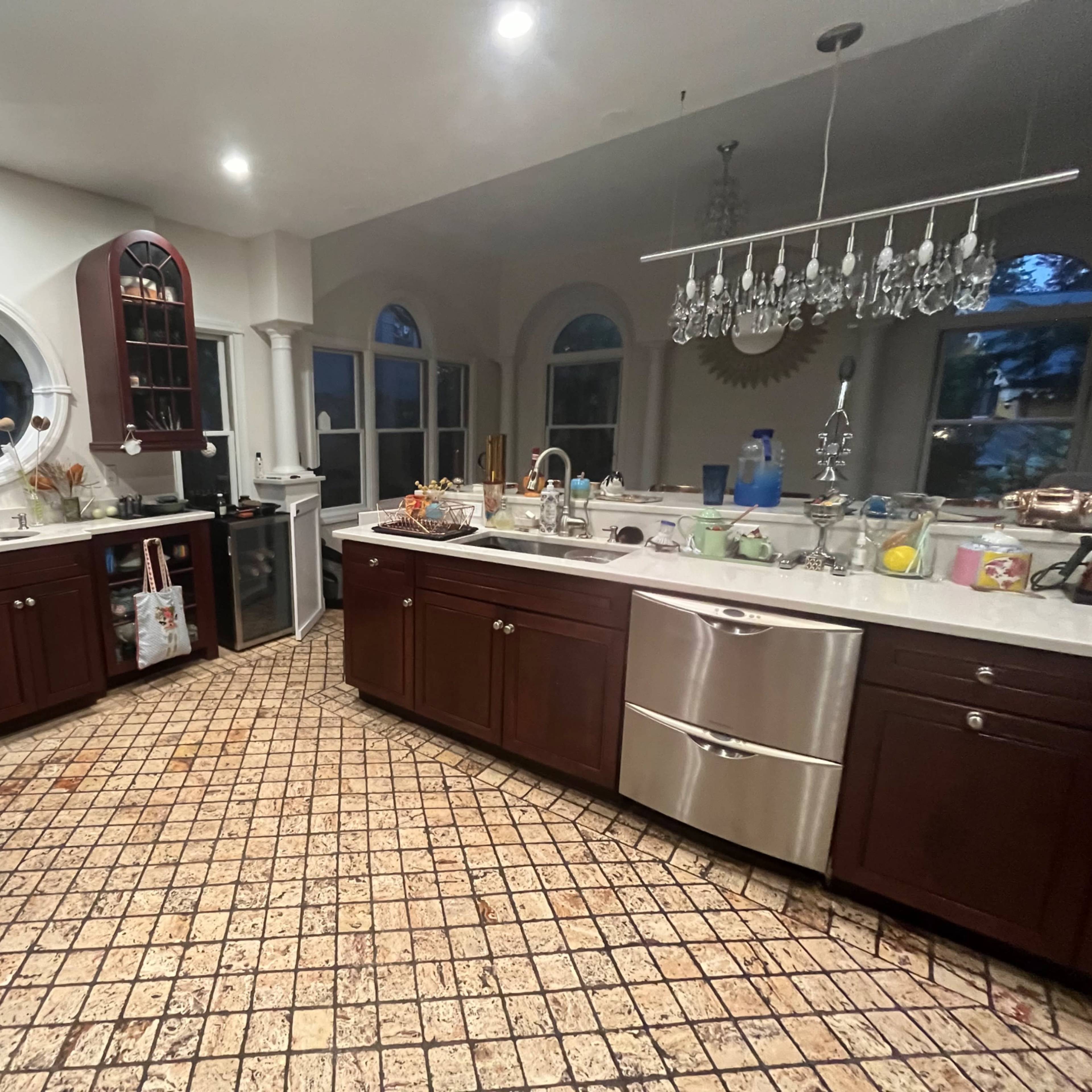 A kitchen with dark wooden cabinets, a stainless steel sink, a marble countertop, and tiled flooring.