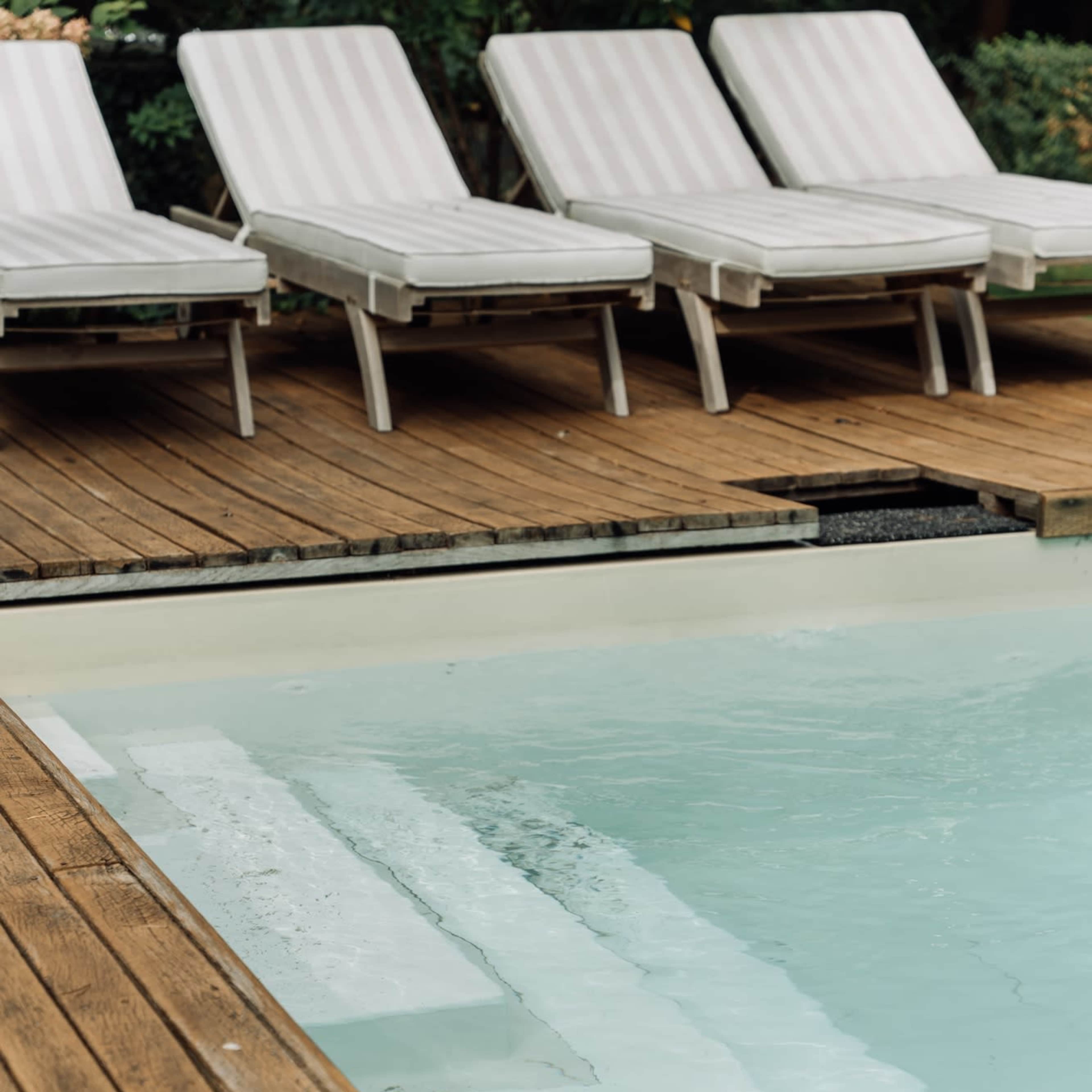 A clear pool with steps leads up to a wooden deck lined with lounge chairs.