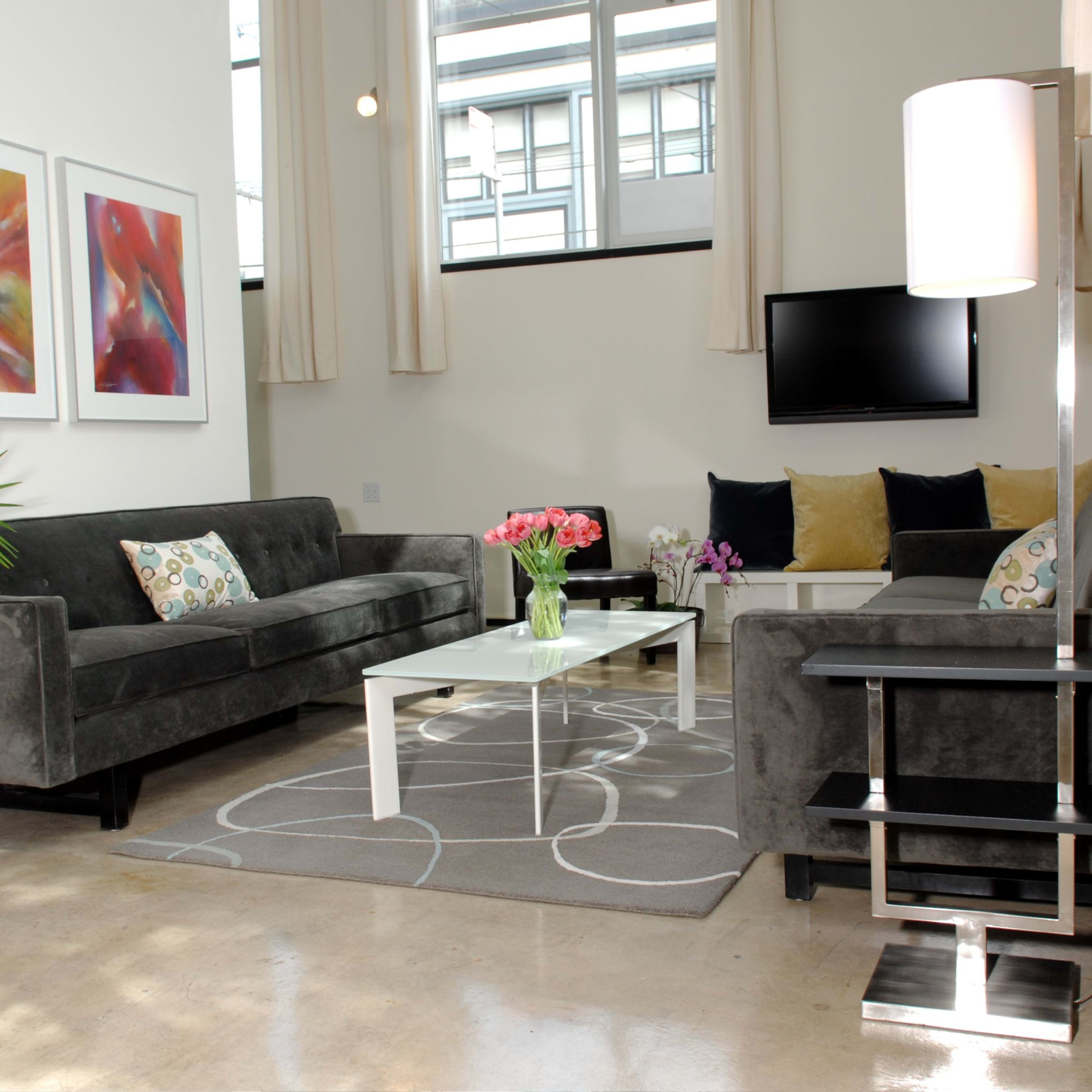 A modern living room featuring two gray sofas facing a coffee table, decorative artwork on the walls, and a vibrant plant in the corner.