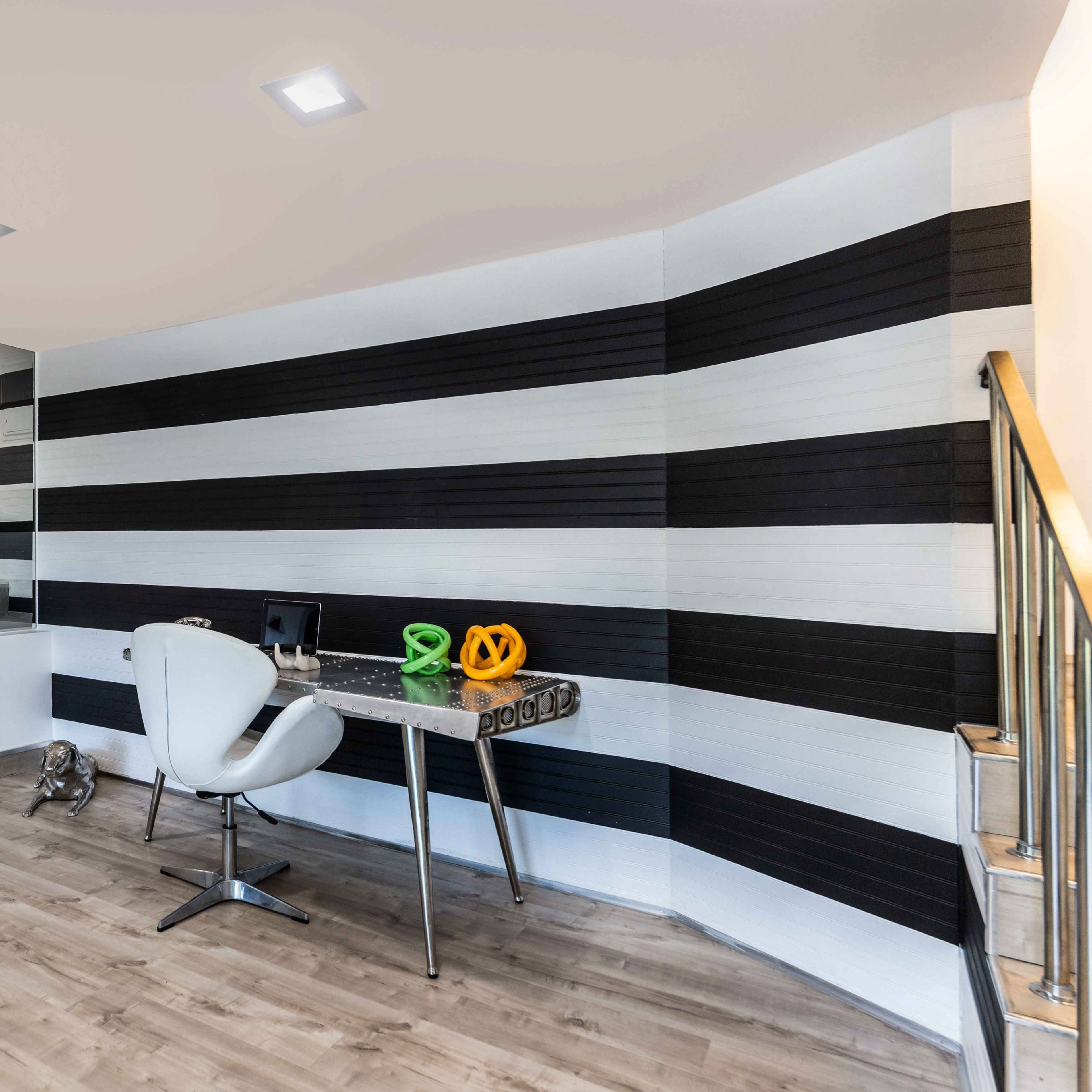 A modern interior space with striped black and white walls, a staircase leading up, a desk with decorative items, and a chair.