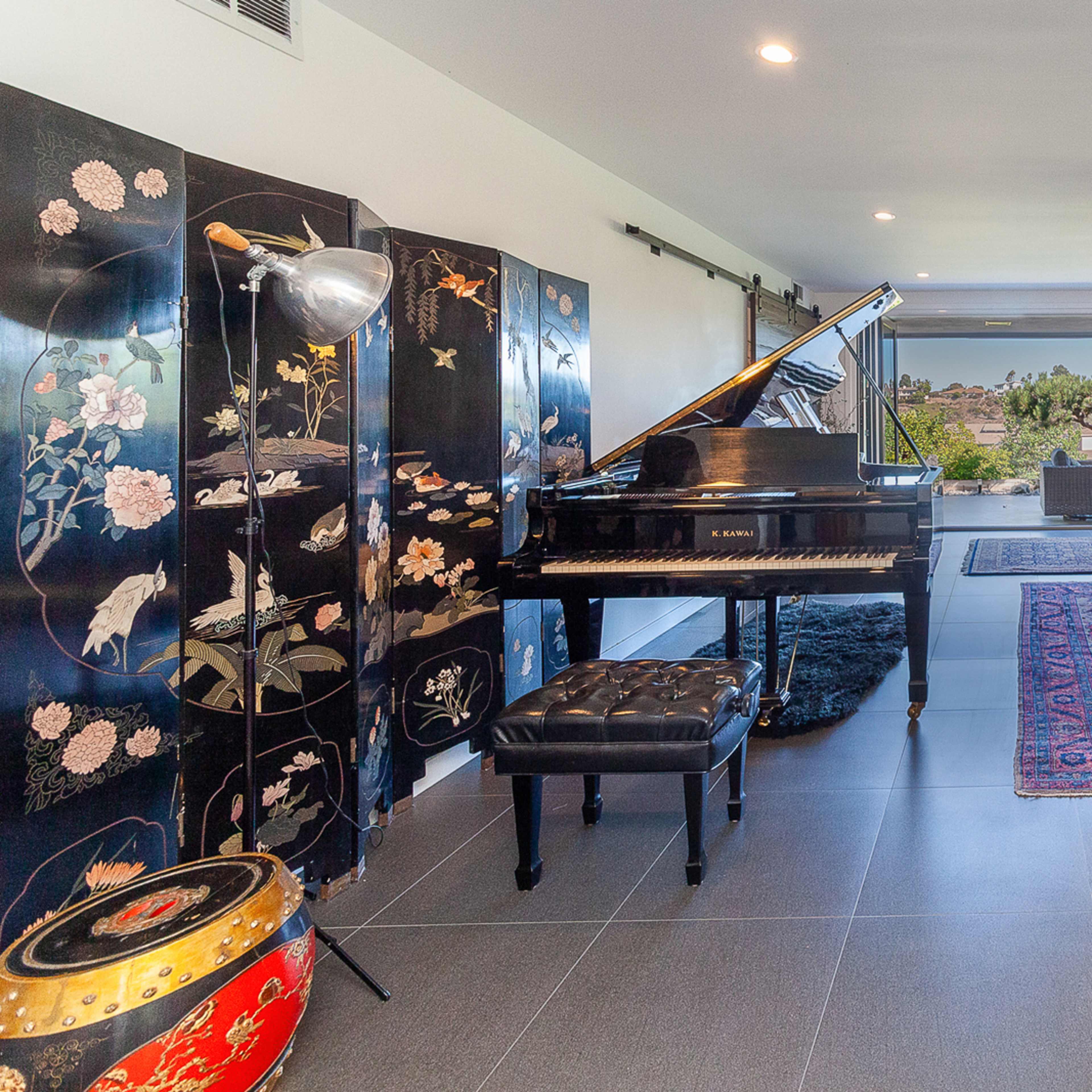 A modern living space featuring a grand piano, a stone fireplace, decorative screens, and a view of the outdoors.