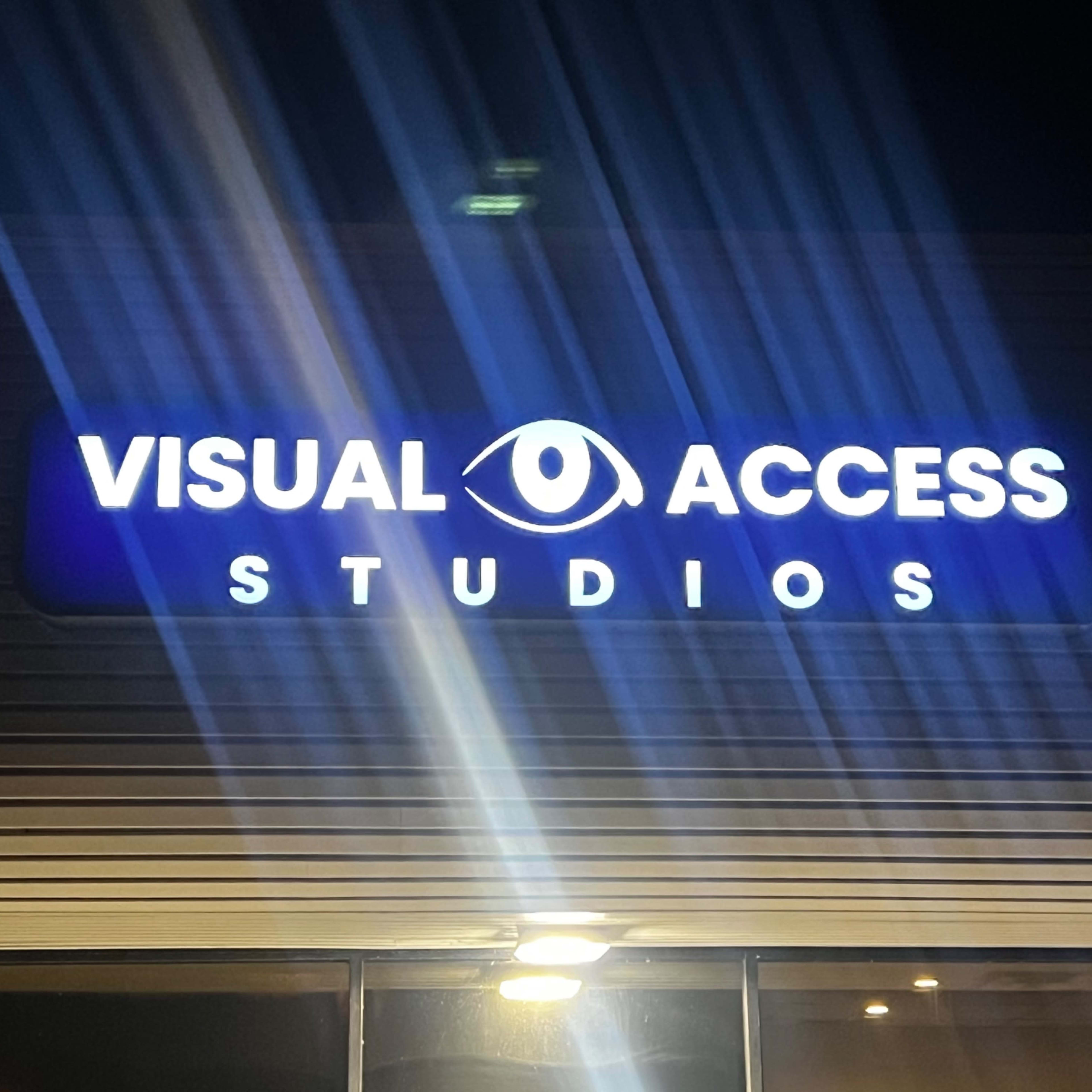 A sign for "Visual Access Studios" illuminated at night, featuring an eye graphic above the name.