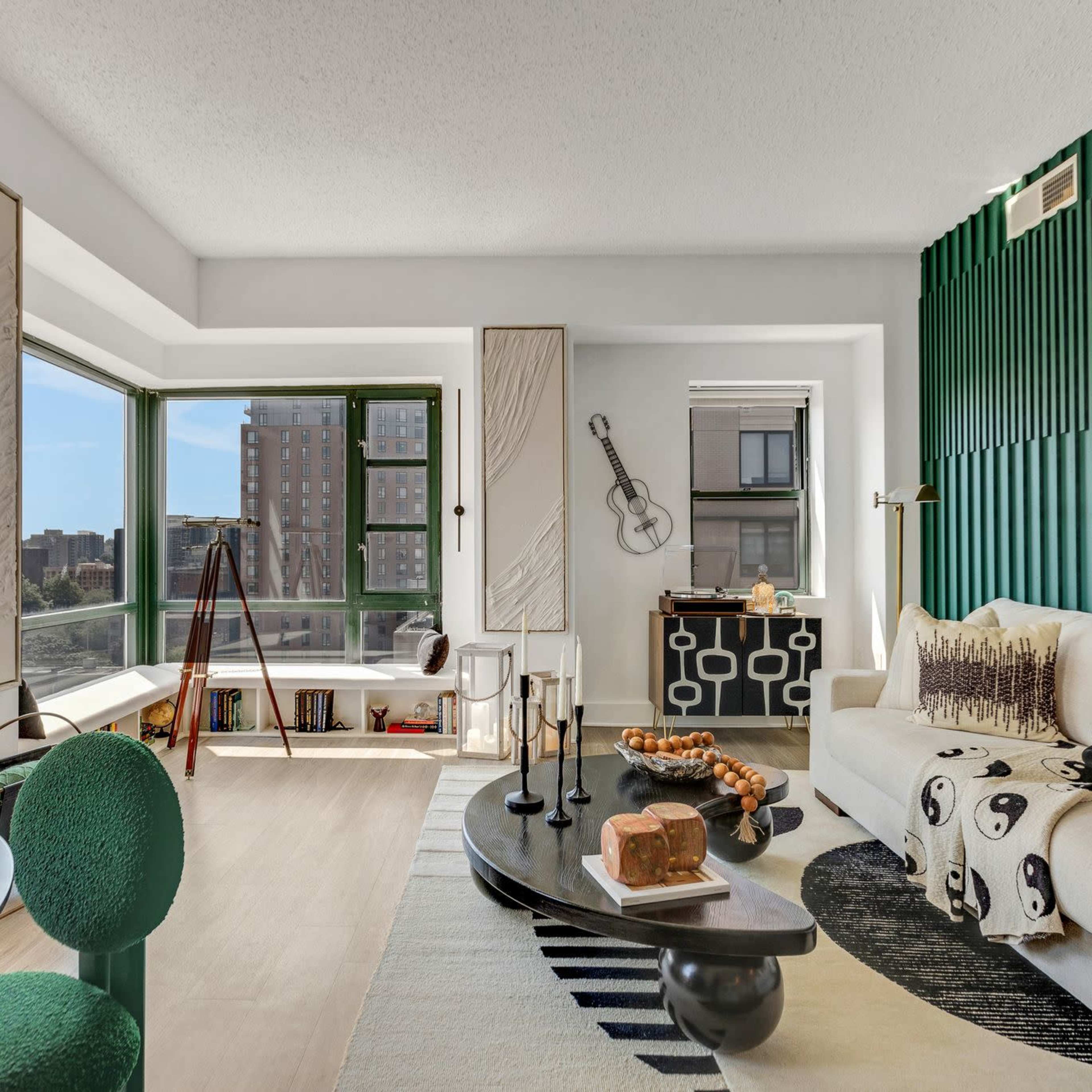 A modern living room with a sectional sofa, a large window offering a city view, and green accent walls.