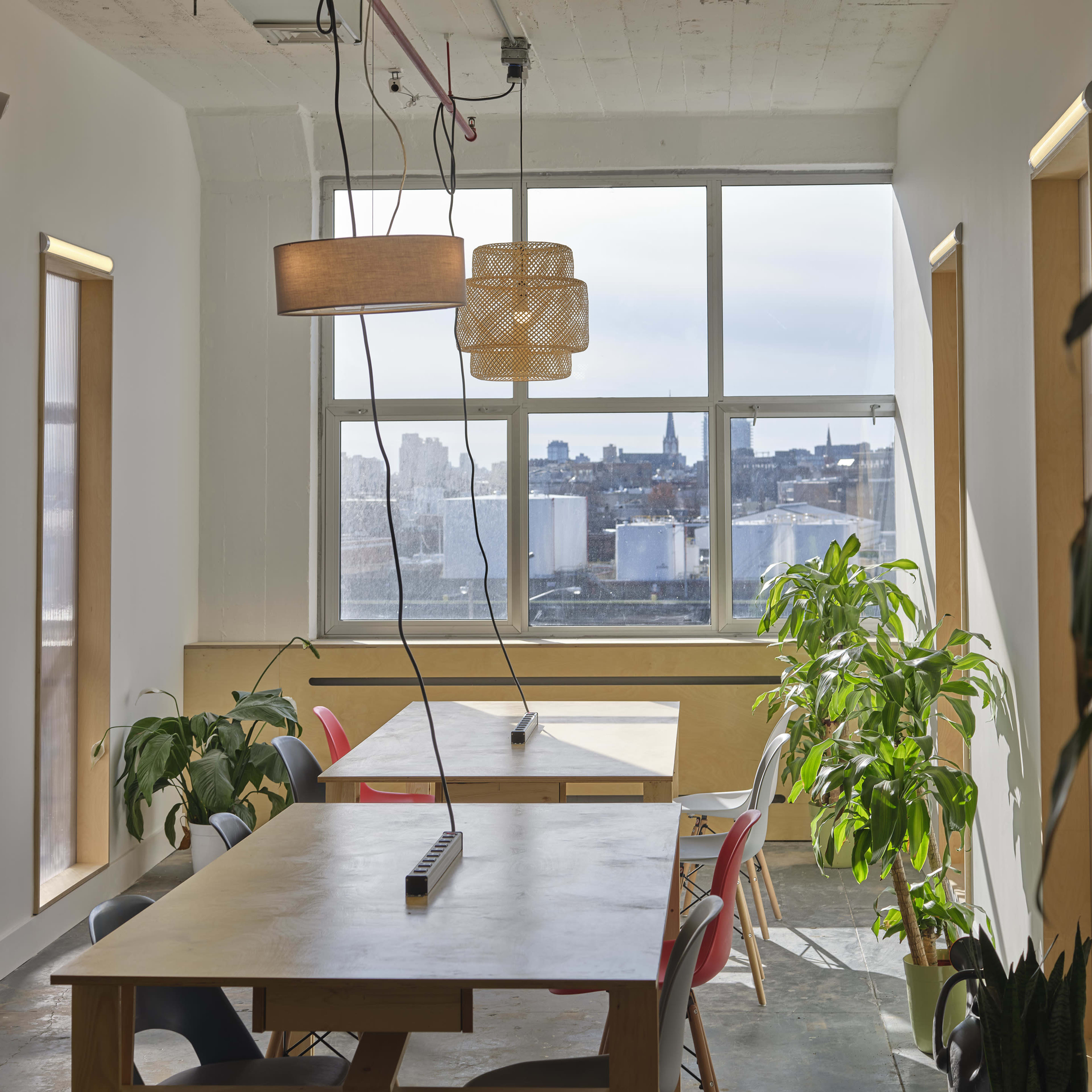 A bright, minimalist office space with tables, plants, and large windows offering a view of the city.