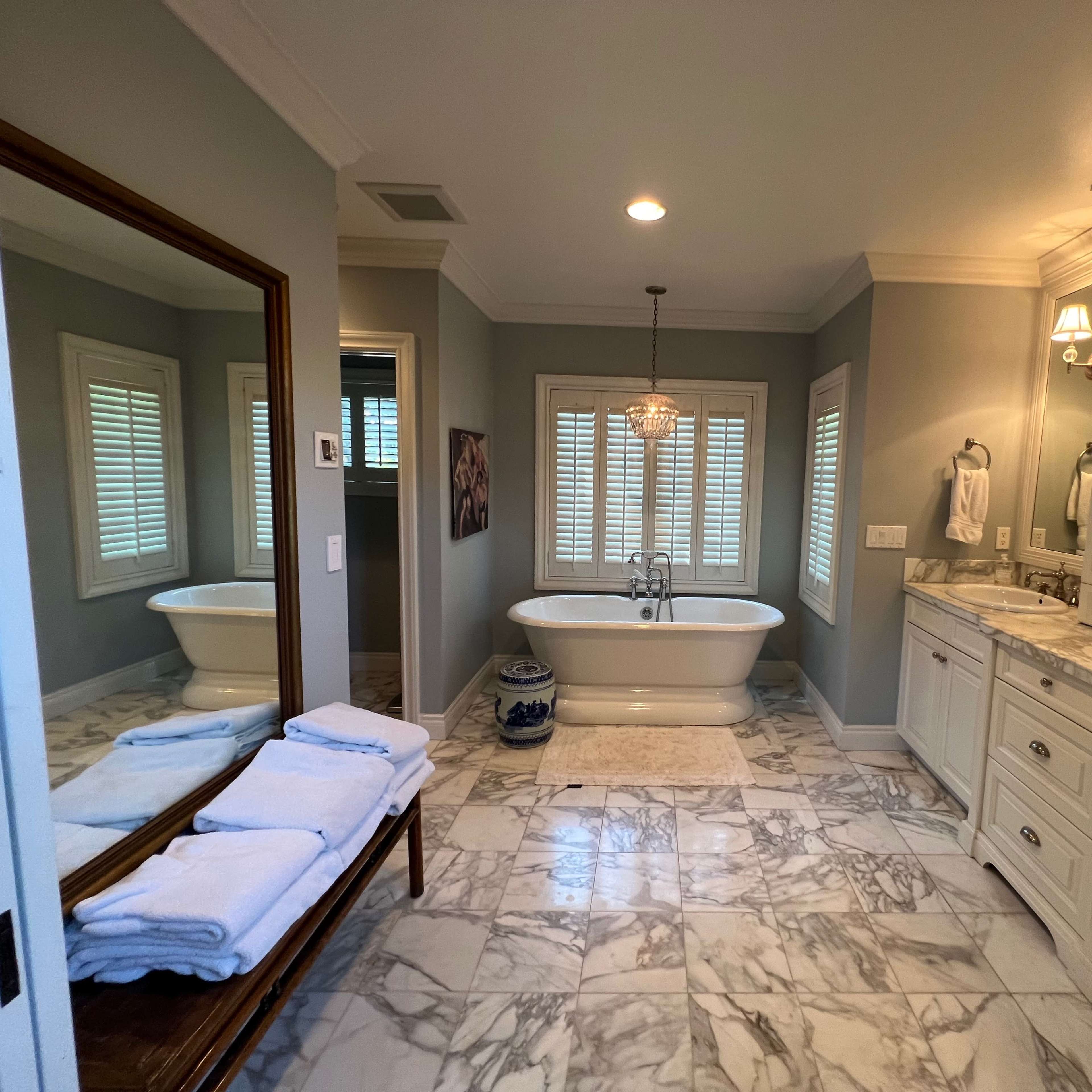 A spacious bathroom featuring a freestanding tub, a double vanity with mirrors, and marble flooring.
